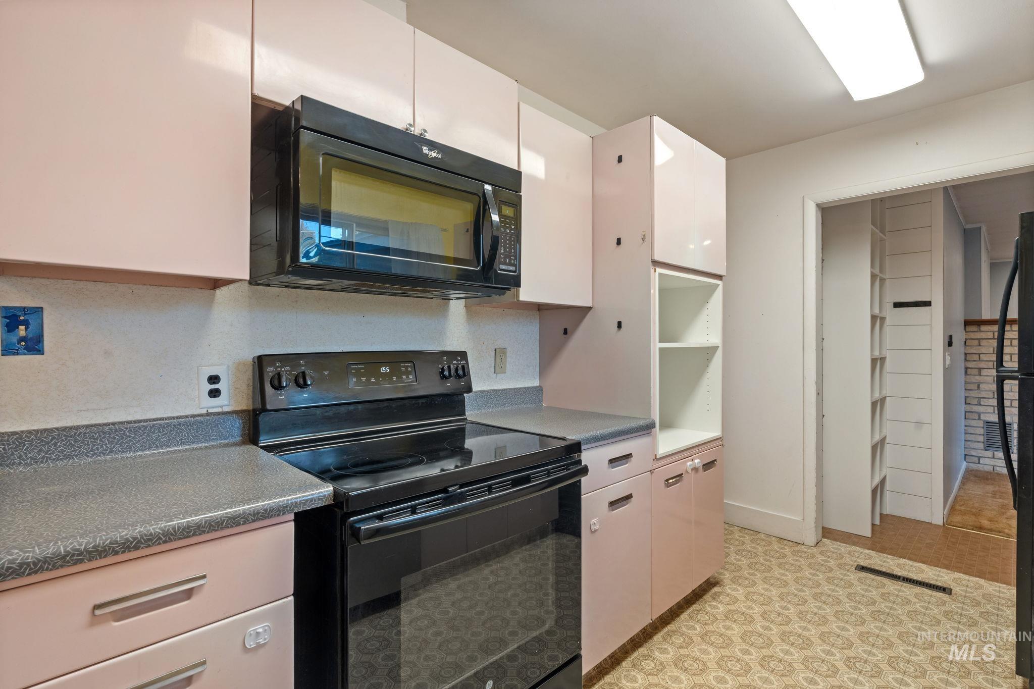 Kitchen with black appliances, dark countertops, white cabinets, and light floors