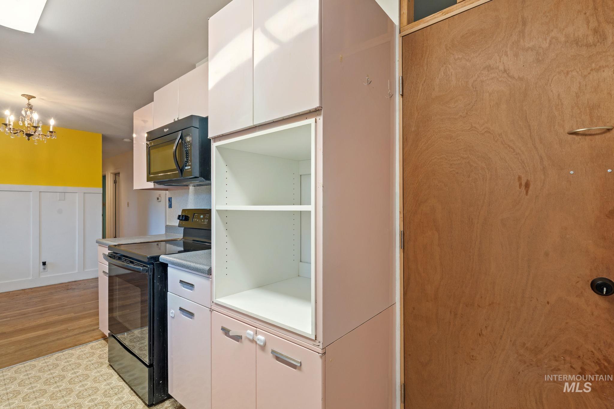 Kitchen with black appliances, white cabinets, a chandelier, modern cabinets, and decorative light fixtures