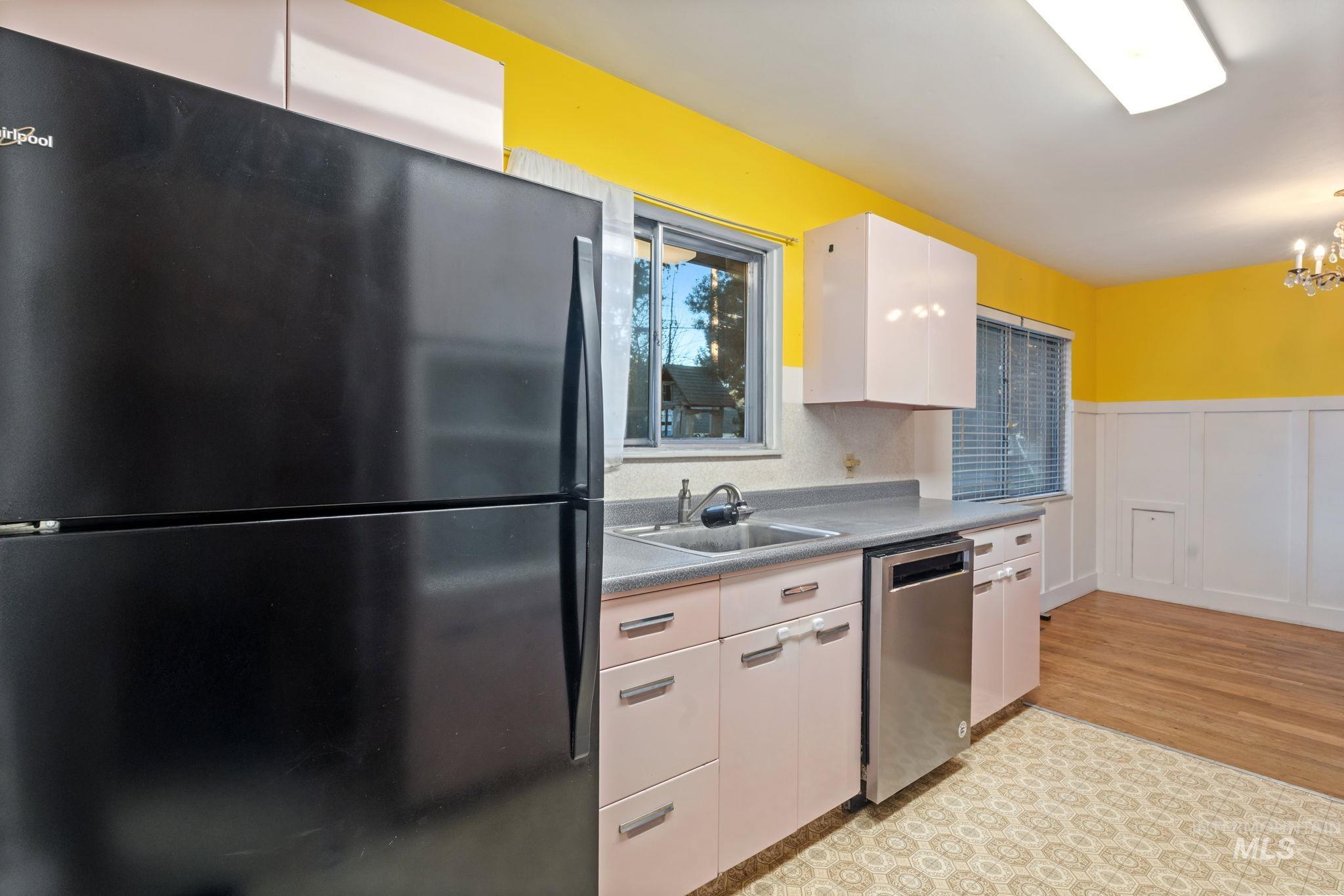 Kitchen featuring freestanding refrigerator, a wainscoted wall, stainless steel dishwasher, dark countertops, and a decorative wall