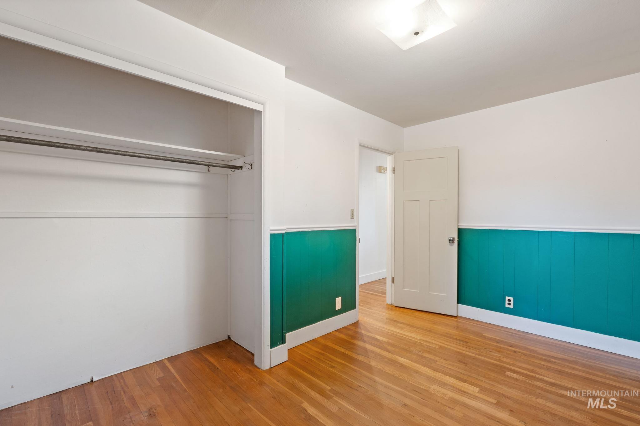 Unfurnished bedroom with wood finished floors, a closet, and wainscoting