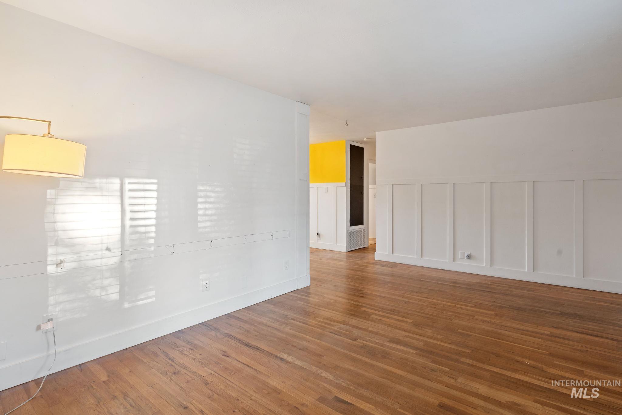 Unfurnished room with a decorative wall, wood finished floors, and wainscoting