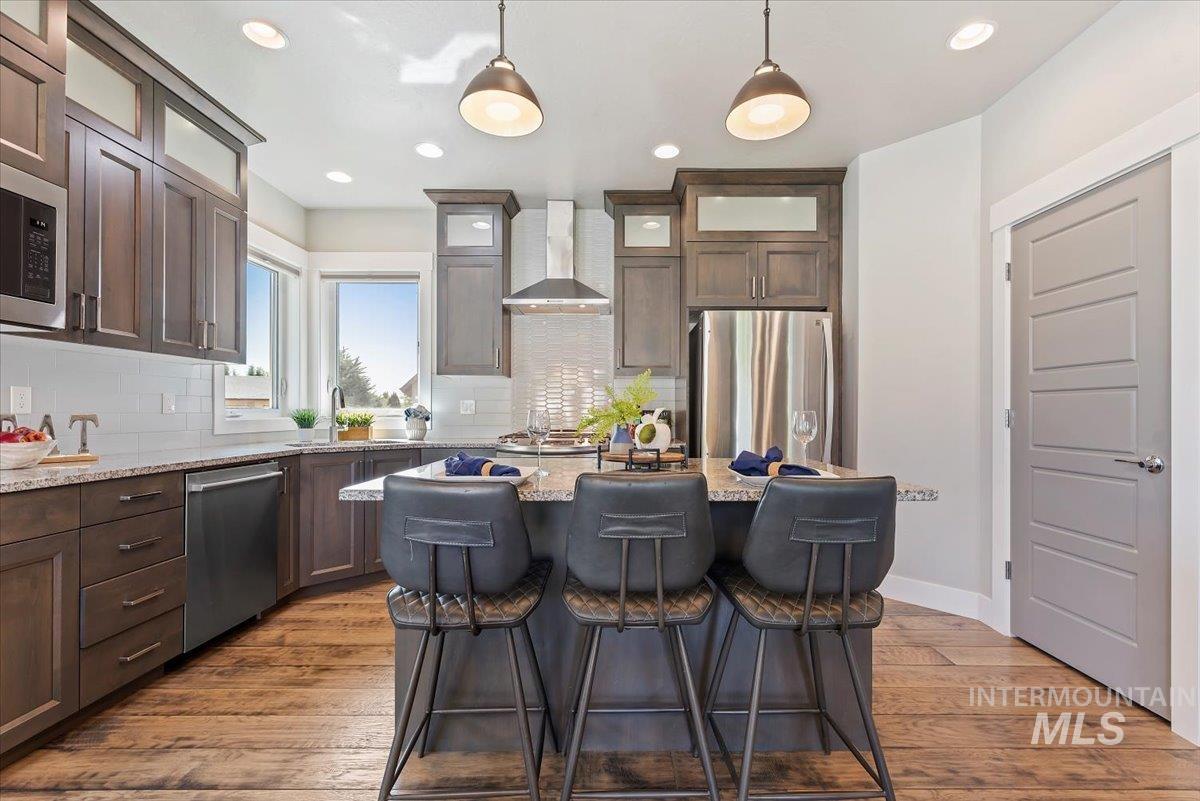 Kitchen featuring dark brown cabinetry, light wood-style flooring, light stone counters, appliances with stainless steel finishes, and decorative light fixtures
