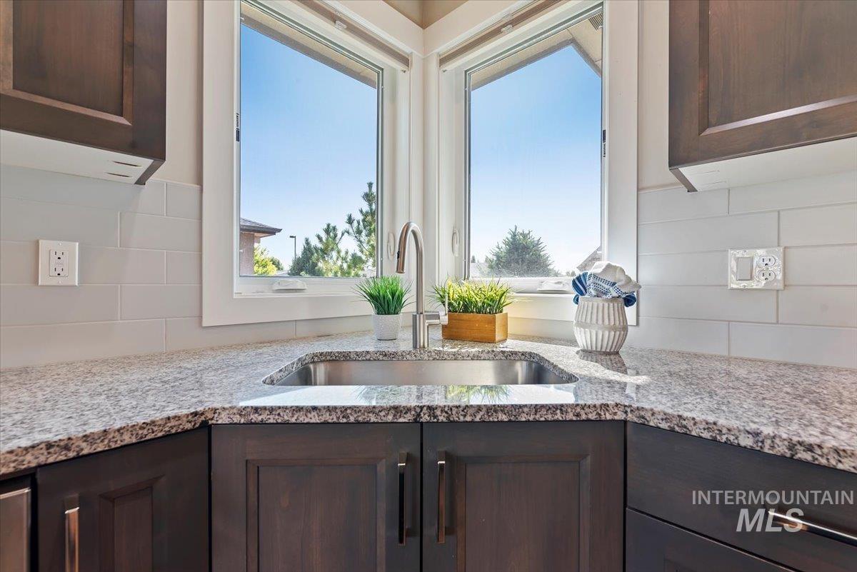 Kitchen featuring dark brown cabinets, decorative backsplash, and light stone countertops
