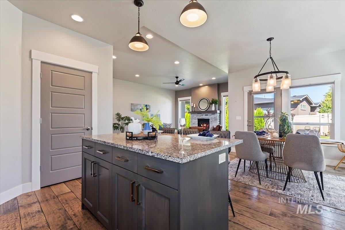 Kitchen with hanging light fixtures, light stone countertops, dark wood-type flooring, a warm lit fireplace, and open floor plan