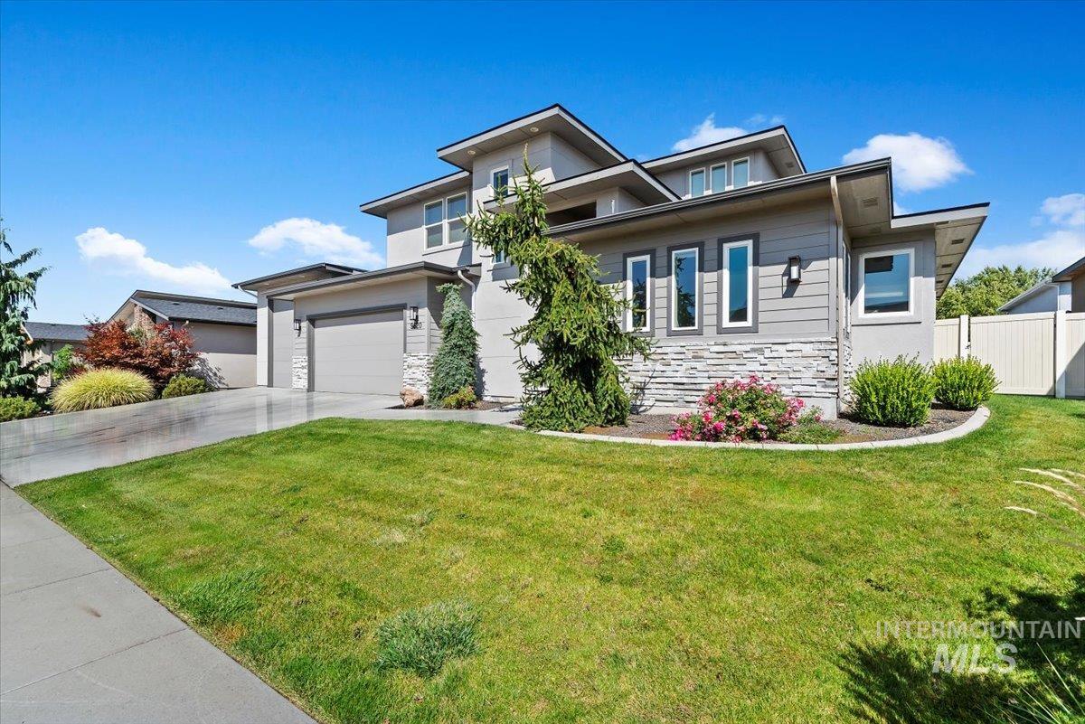 View of front of home featuring stone siding, a garage, concrete driveway, and a front lawn