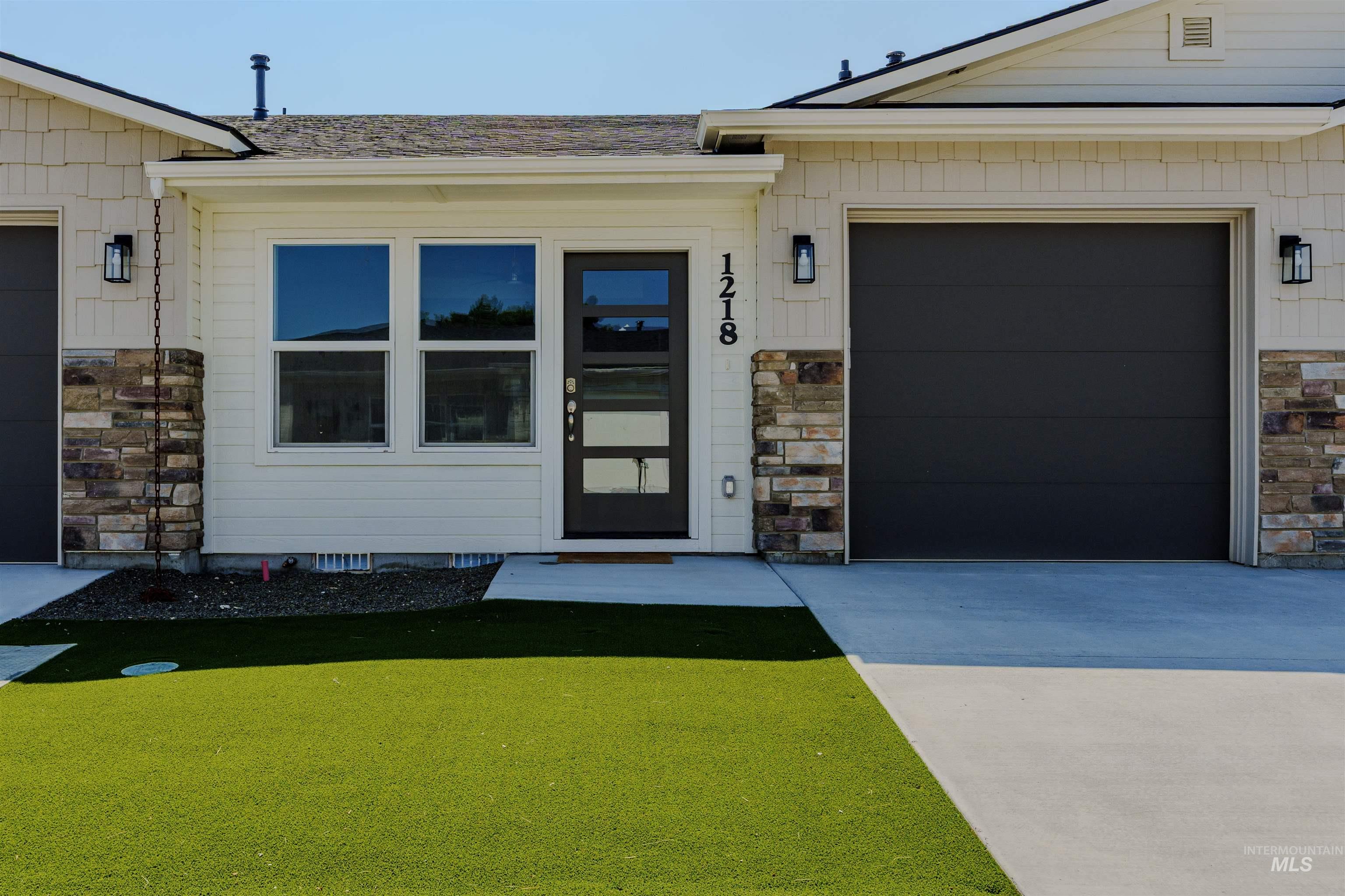 View of exterior entry featuring stone siding, concrete driveway, and a lawn
