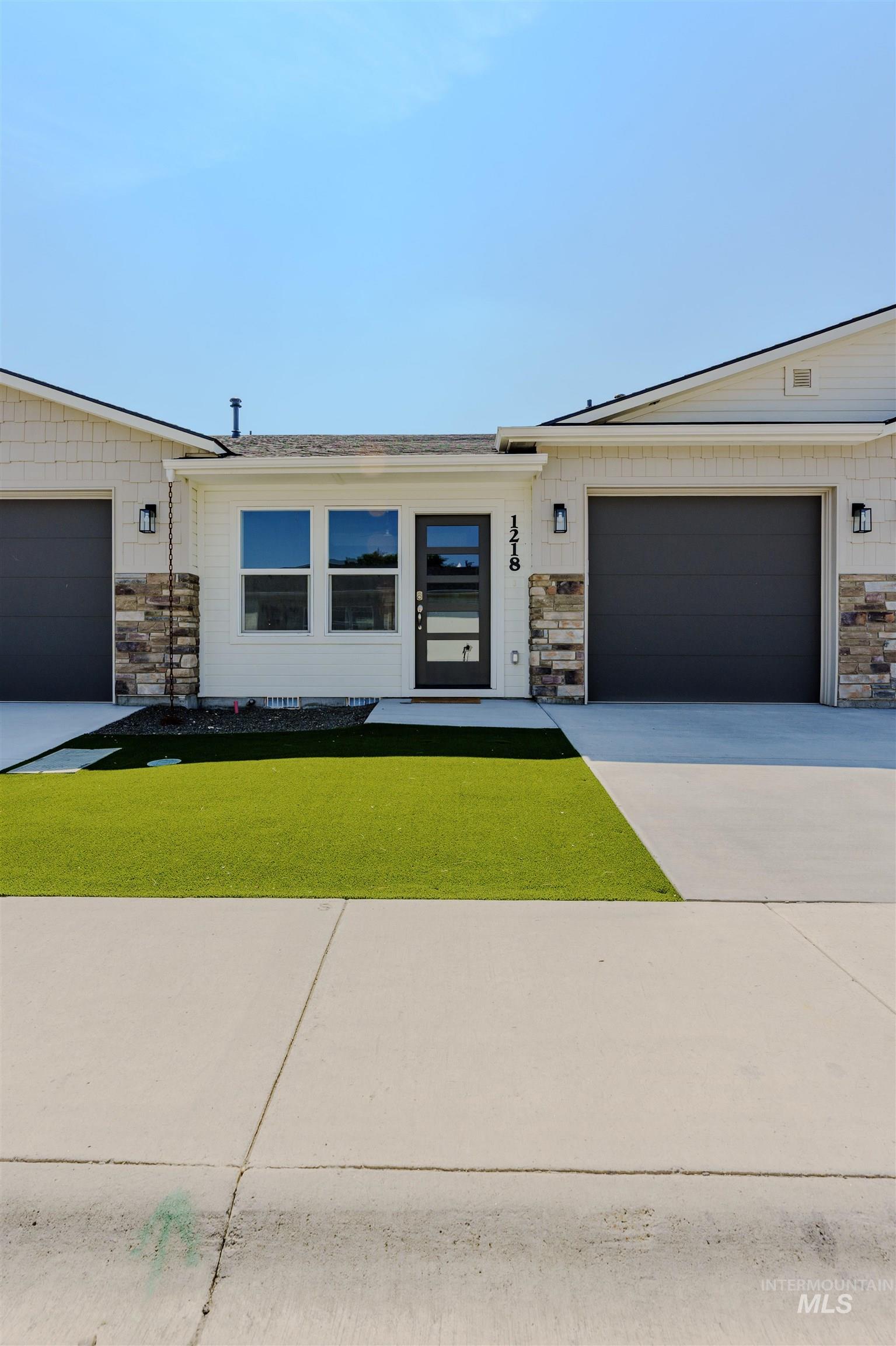 View of front of property featuring stone siding, concrete driveway, a front lawn, and an attached garage