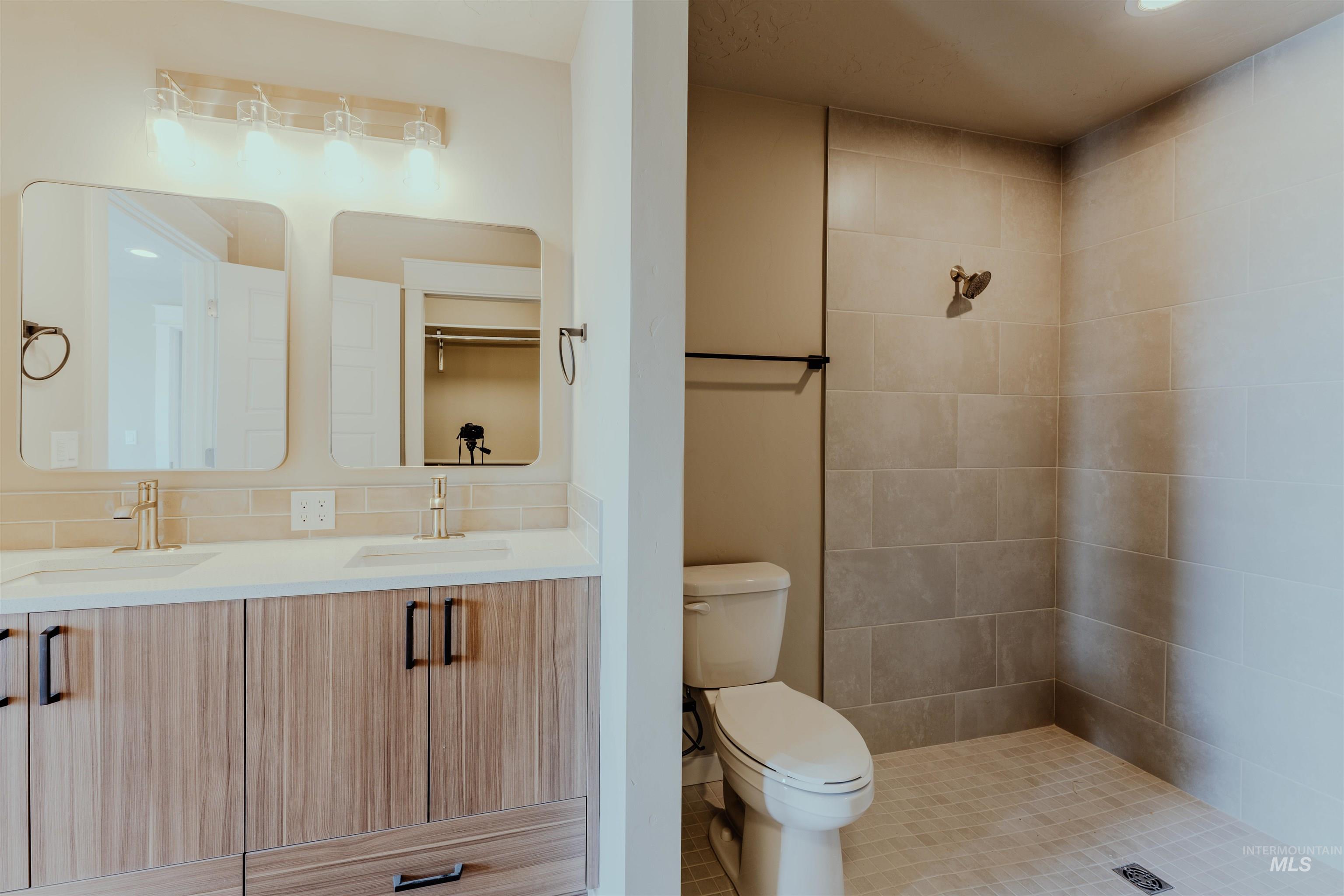 Bathroom featuring double vanity, tiled shower, and a closet