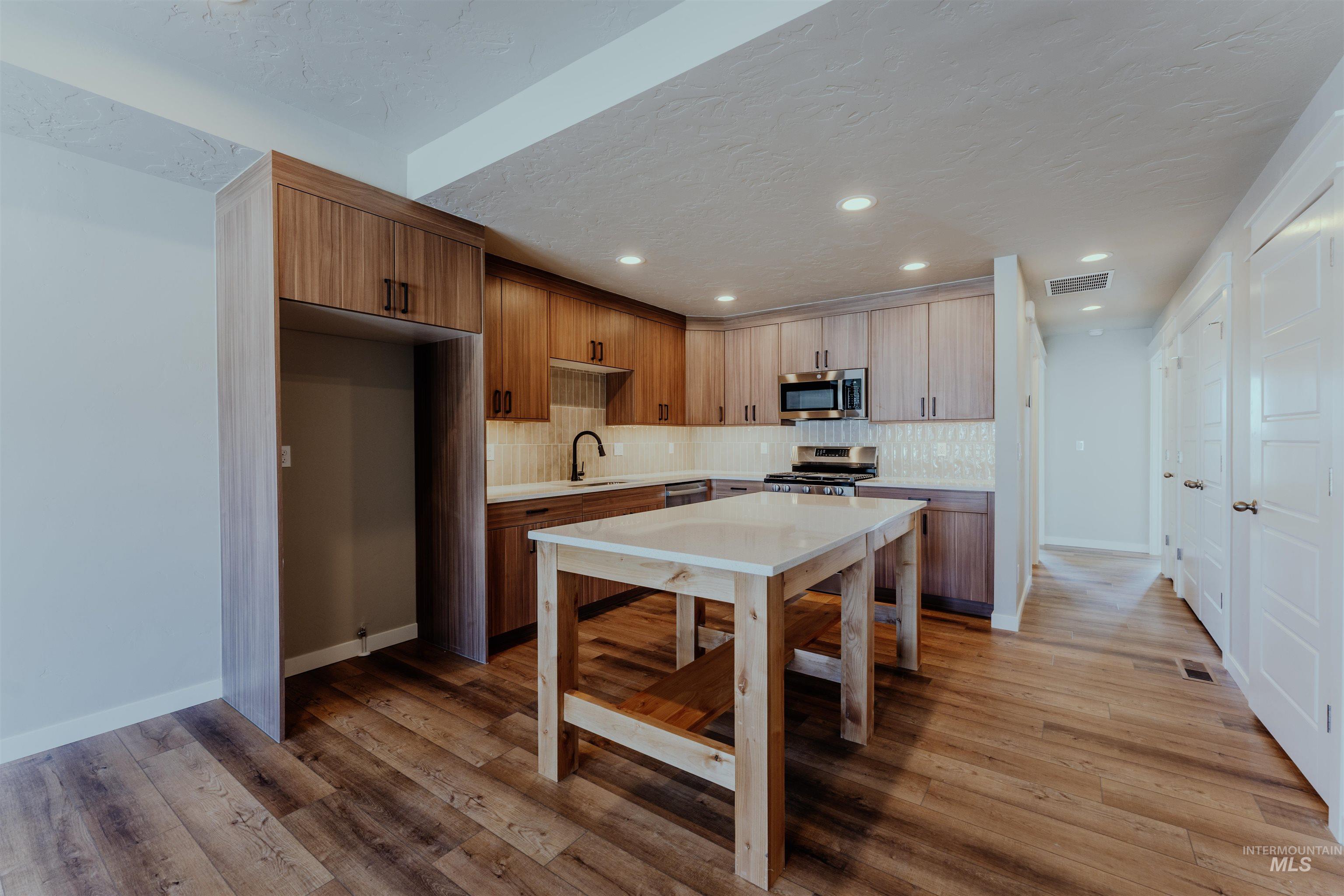 Kitchen featuring brown cabinets, modern cabinets, light wood-style flooring, a textured ceiling, and appliances with stainless steel finishes