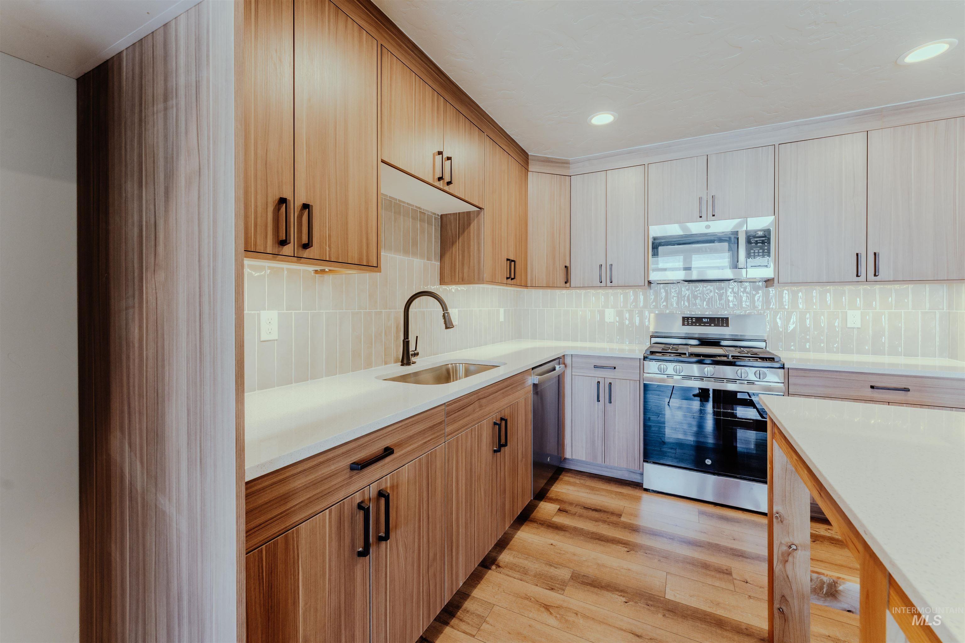 Kitchen featuring tasteful backsplash, stainless steel appliances, light wood-style flooring, light stone countertops, and light brown cabinetry