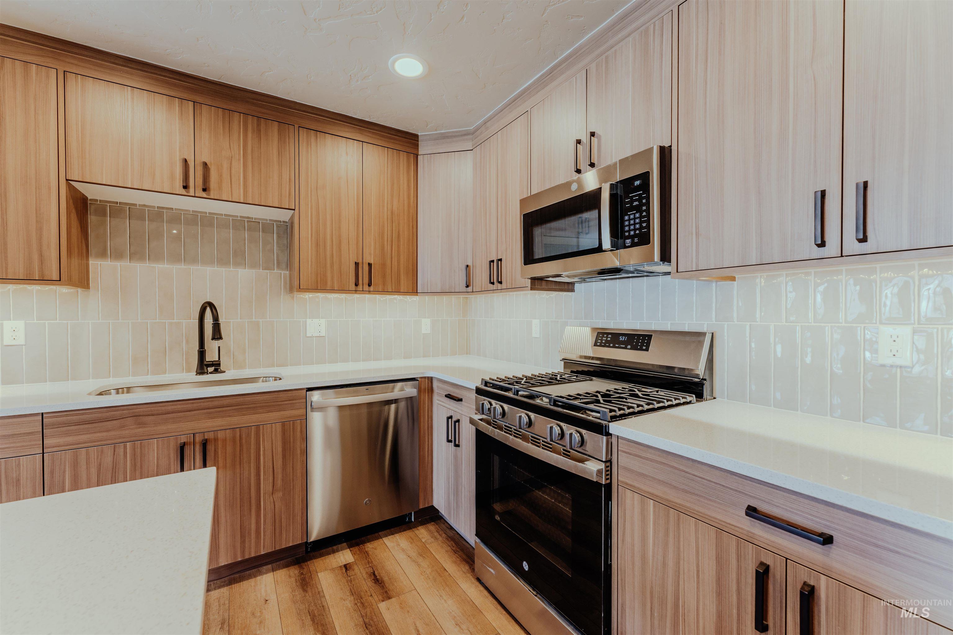 Kitchen with appliances with stainless steel finishes, decorative backsplash, light wood-style flooring, light stone countertops, and light brown cabinets