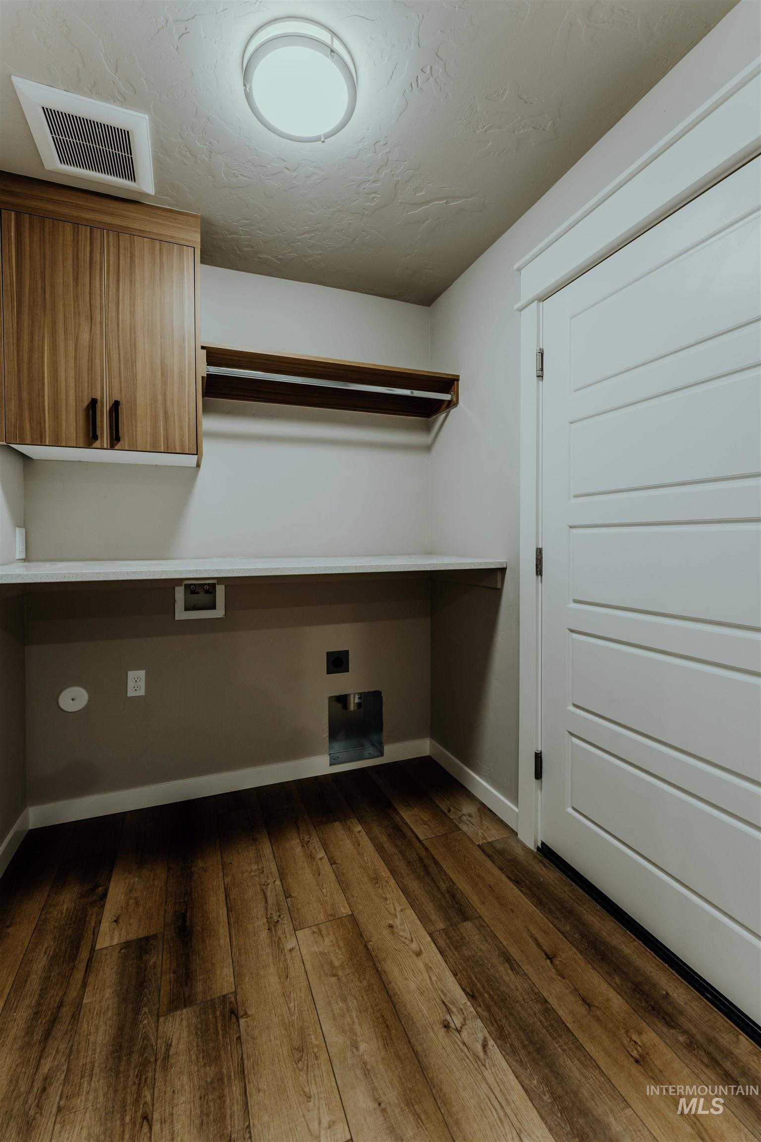 Laundry room featuring dark wood-type flooring, cabinet space, a textured ceiling, hookup for a washing machine, and electric dryer hookup