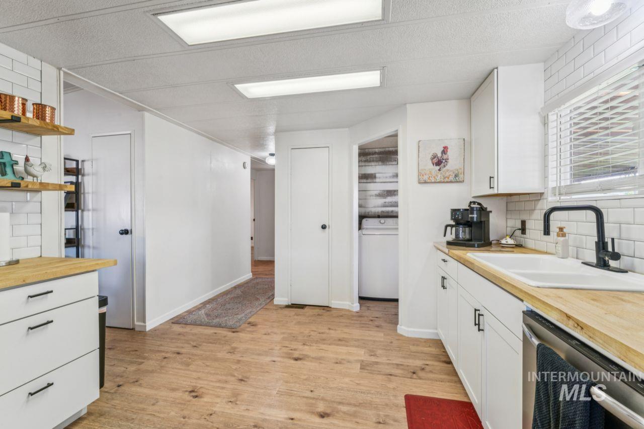 Kitchen with decorative backsplash, wooden counters, dishwasher, light wood-style flooring, and white cabinets