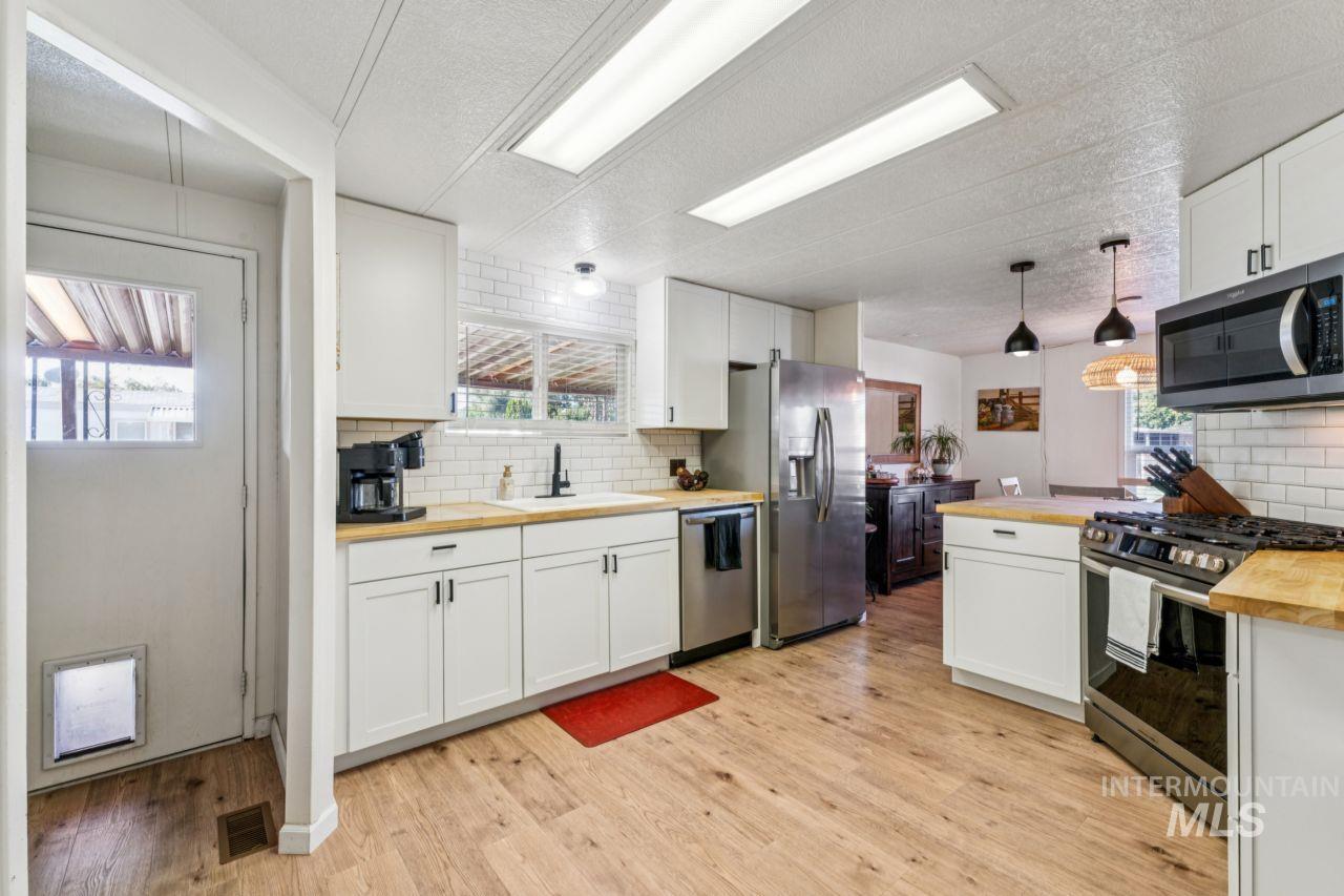 Kitchen featuring wooden counters, decorative backsplash, appliances with stainless steel finishes, white cabinets, and a textured ceiling