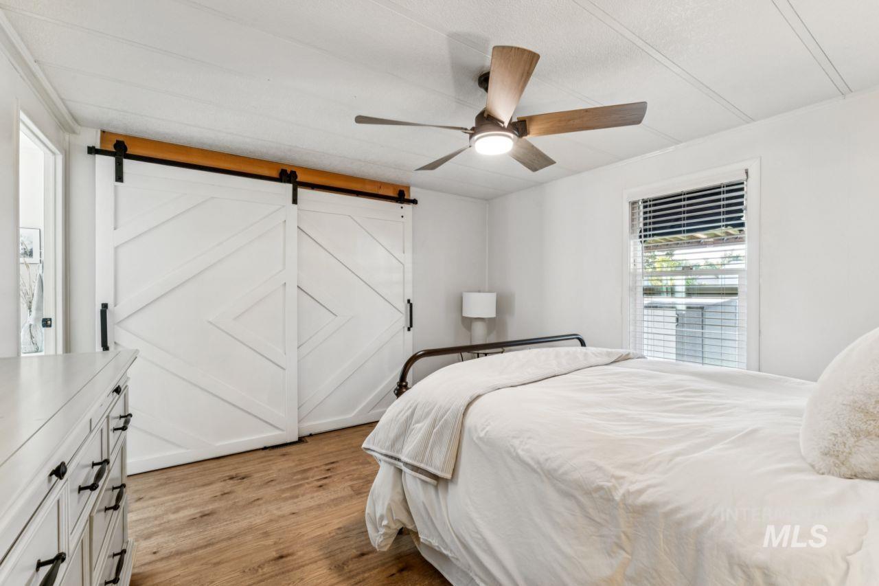 Bedroom with light wood-style floors, ceiling fan, and a barn door