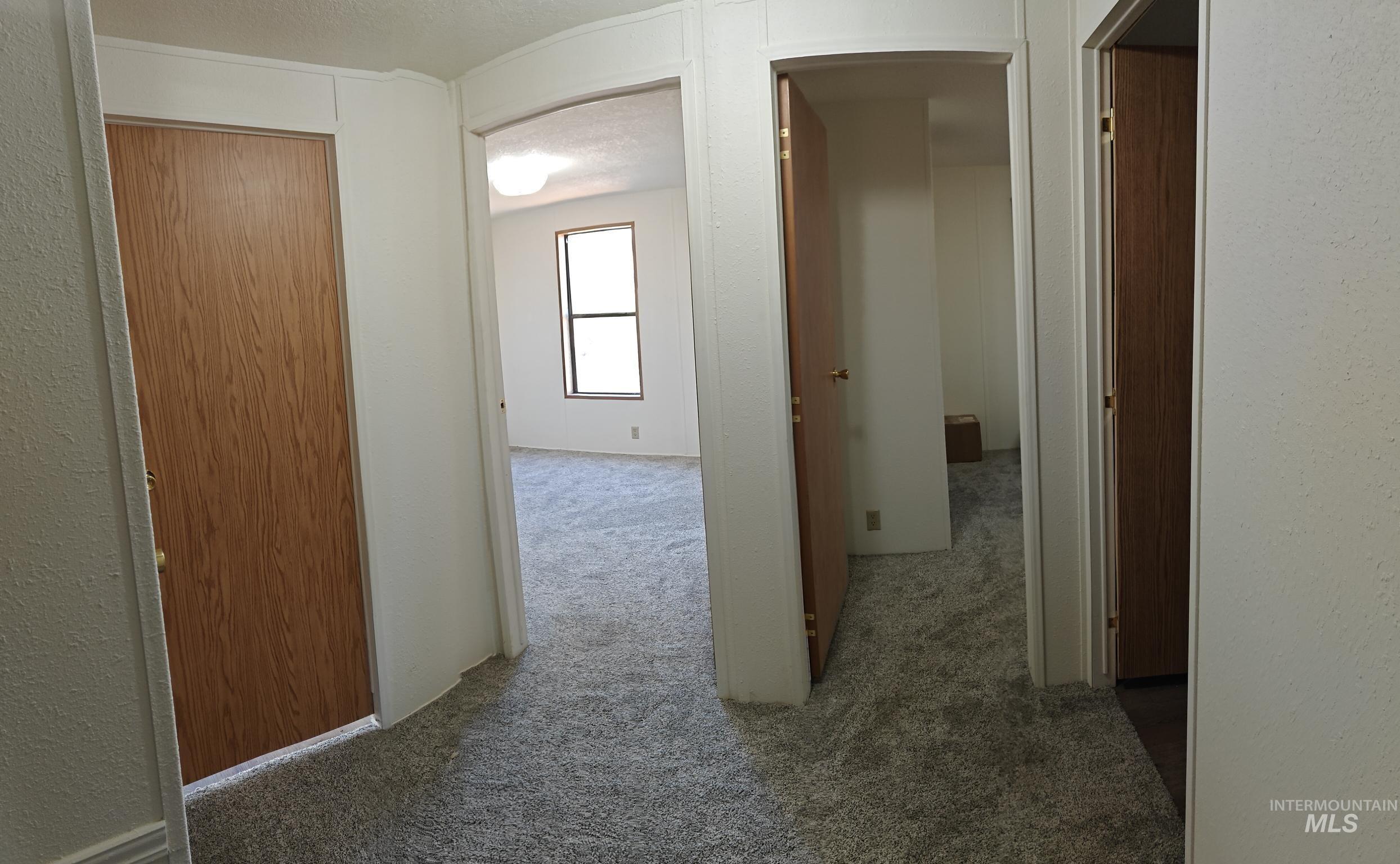 Corridor featuring a textured wall, carpet flooring, and a textured ceiling