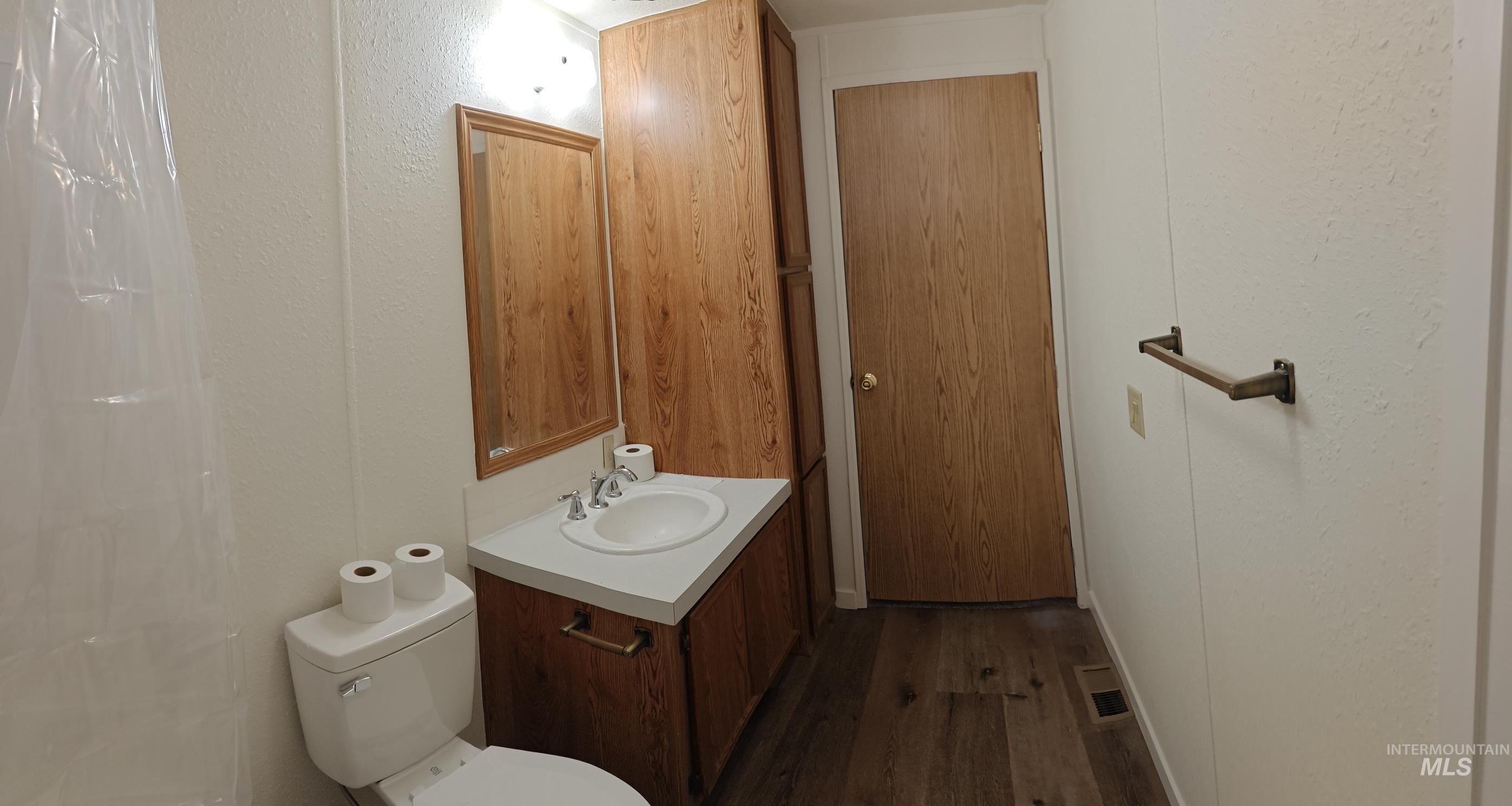 Full bathroom featuring dark wood-style flooring, vanity, a textured wall, and a shower with shower curtain