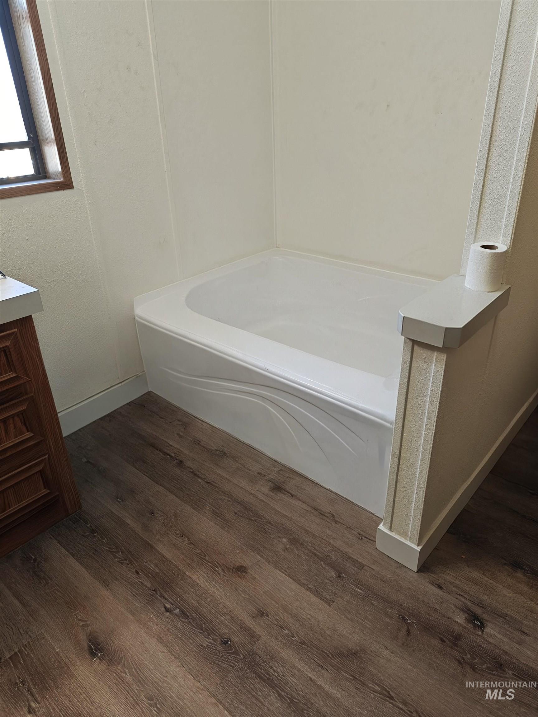 Bathroom featuring a garden tub, vanity, dark wood finished floors, and a textured wall