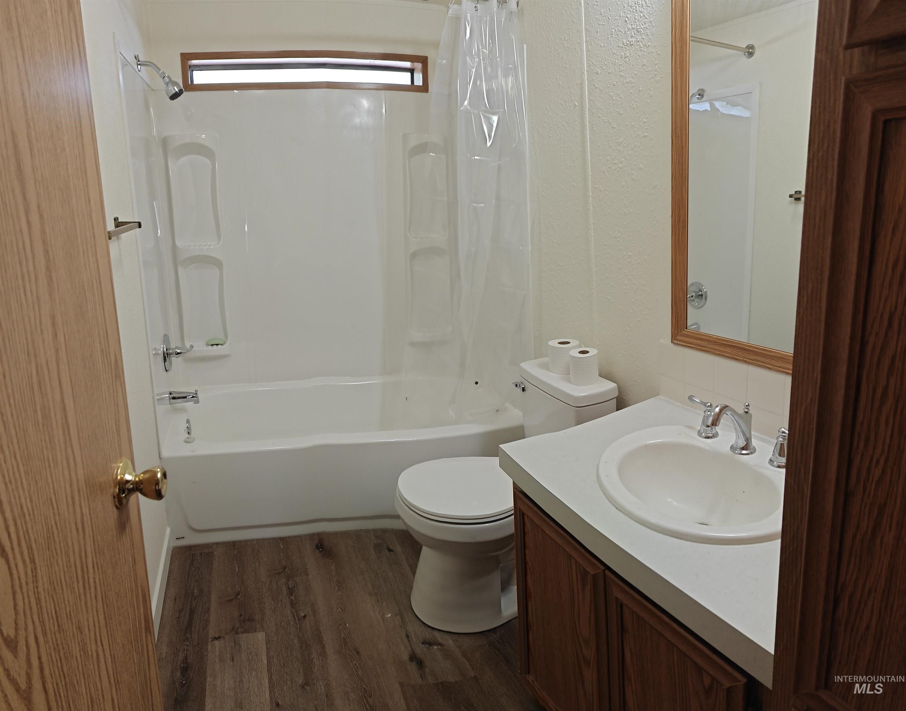Bathroom with shower / bath combination with curtain, dark wood-style floors, vanity, and a textured wall