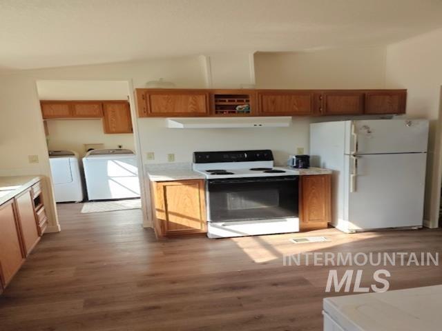 Kitchen with white appliances, light countertops, washer and dryer, and light wood-style flooring