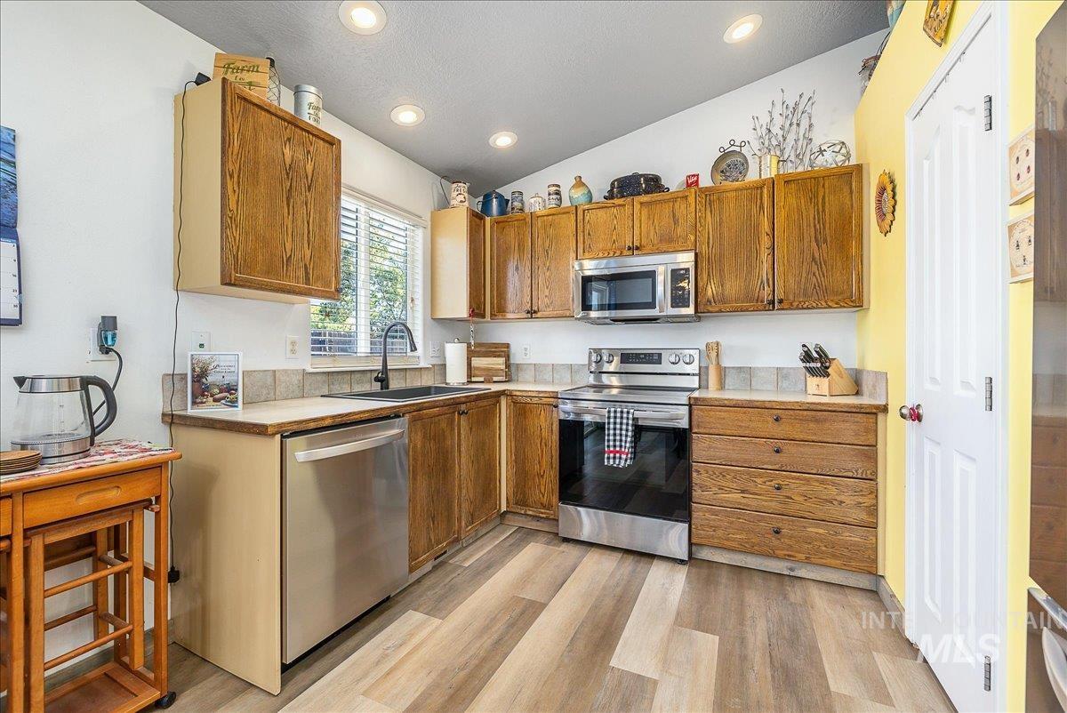 Bright and cheery kitchen.  Appliances have stainless steel finishes, light countertops, vaulted ceiling, and recessed lighting and a pretty picture window looking onto the backyard.