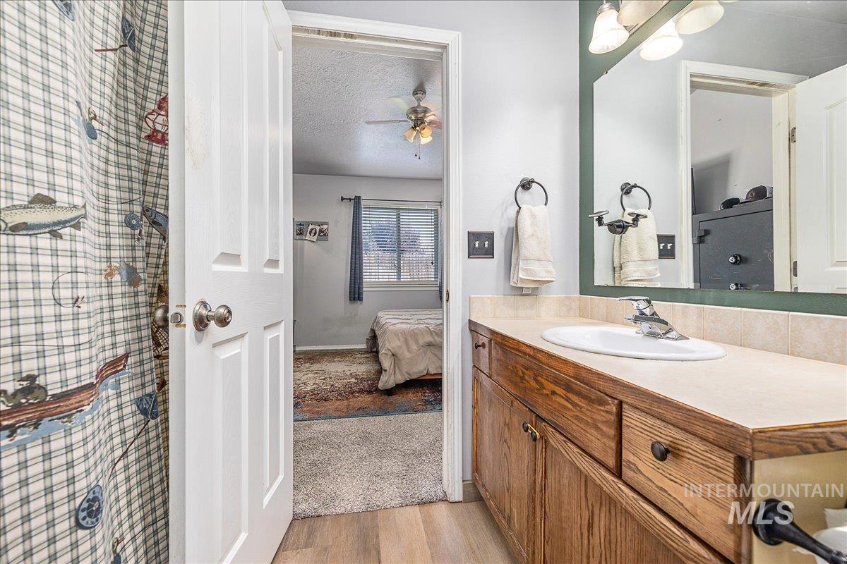 Primary bathroom with vanity, shower-tub combo and light wood-style flooring.
