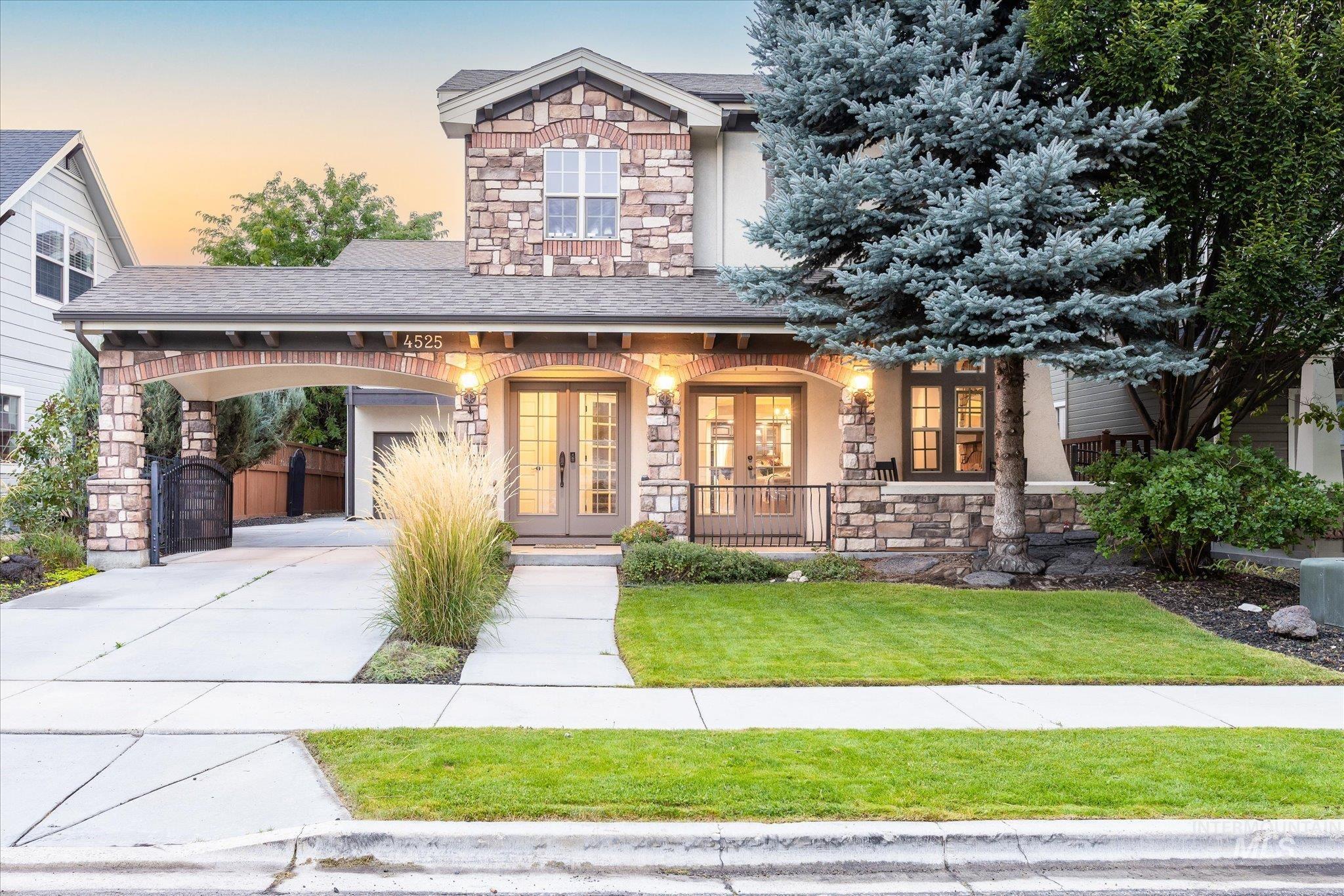 View of front of property featuring stone siding, french doors, covered porch, driveway, and a front lawn