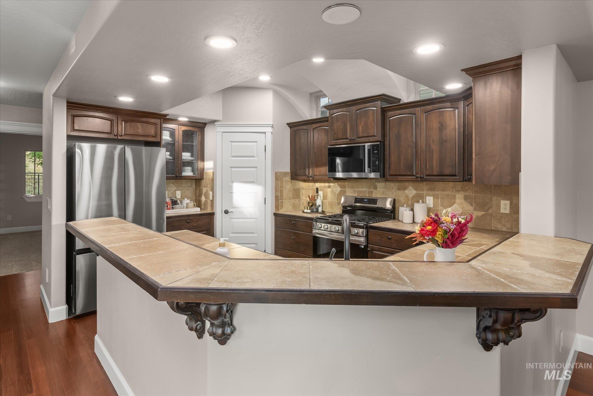 Kitchen featuring tasteful backsplash, dark wood-style flooring, a kitchen breakfast bar, appliances with stainless steel finishes, and recessed lighting