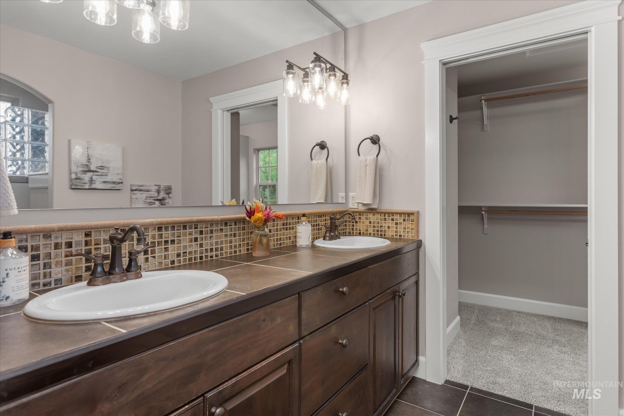 Bathroom with decorative backsplash, double vanity, a spacious closet, and dark tile patterned floors