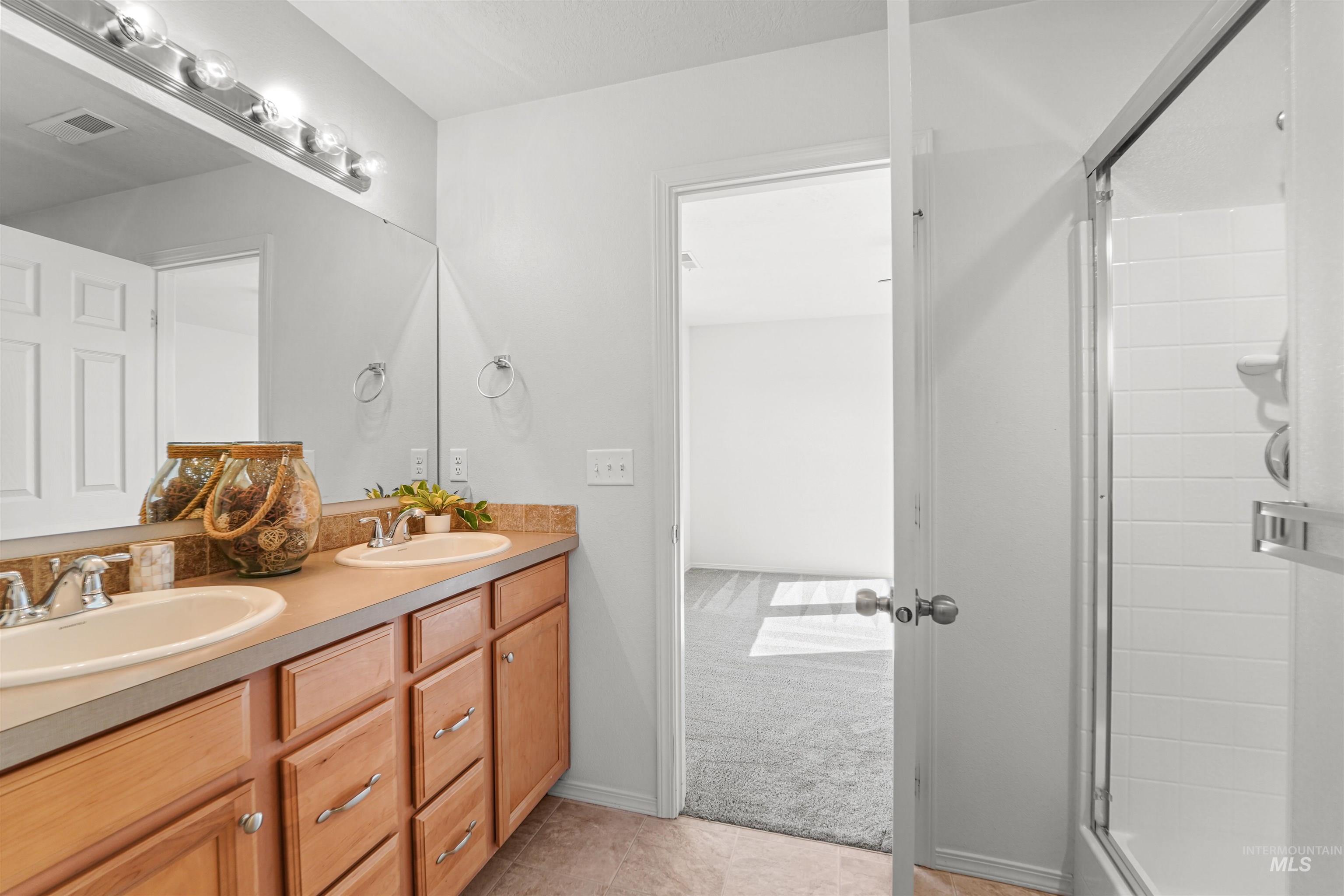 Bathroom featuring a stall shower, double vanity, and light tile patterned floors