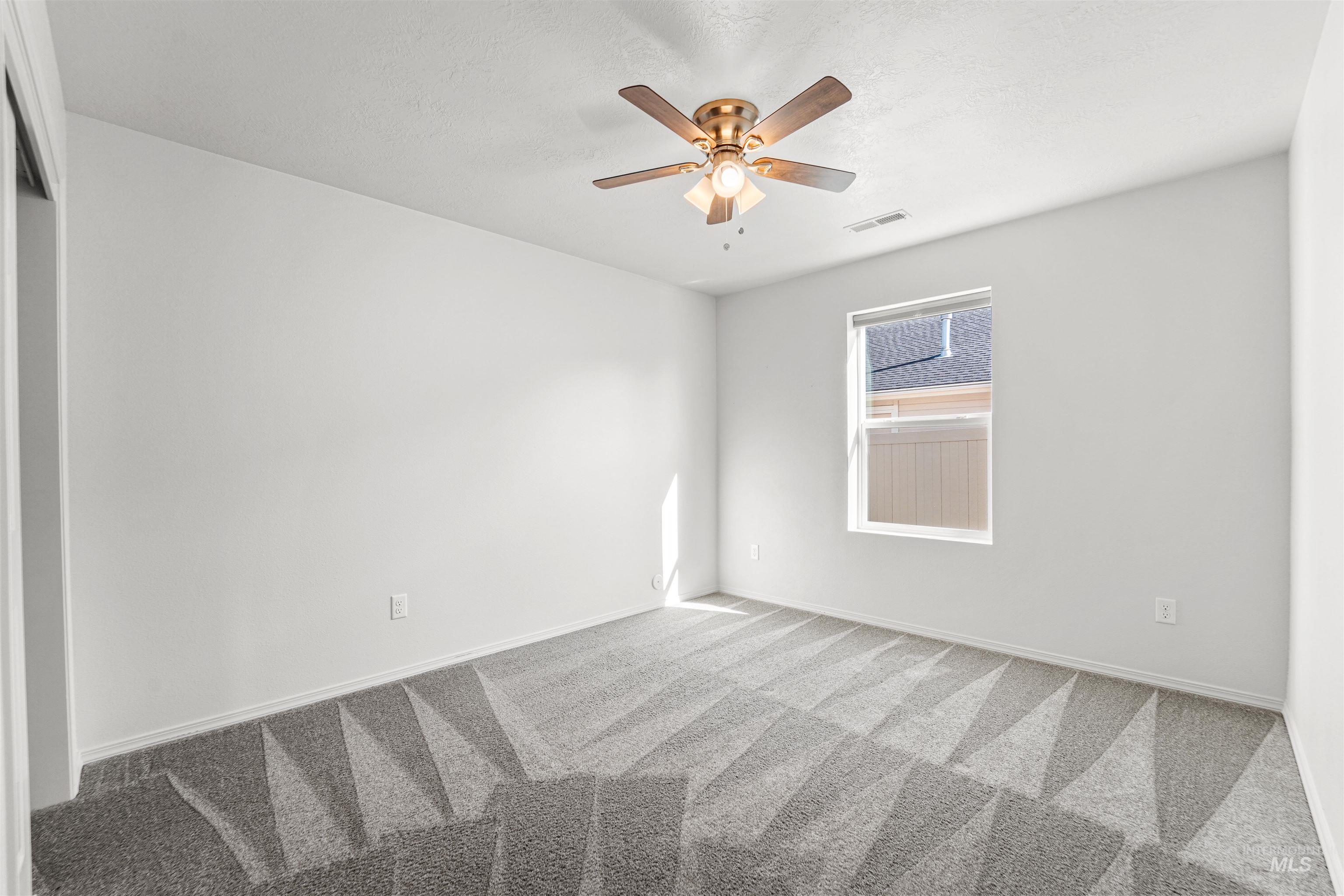 Carpeted empty room with a textured ceiling and a ceiling fan