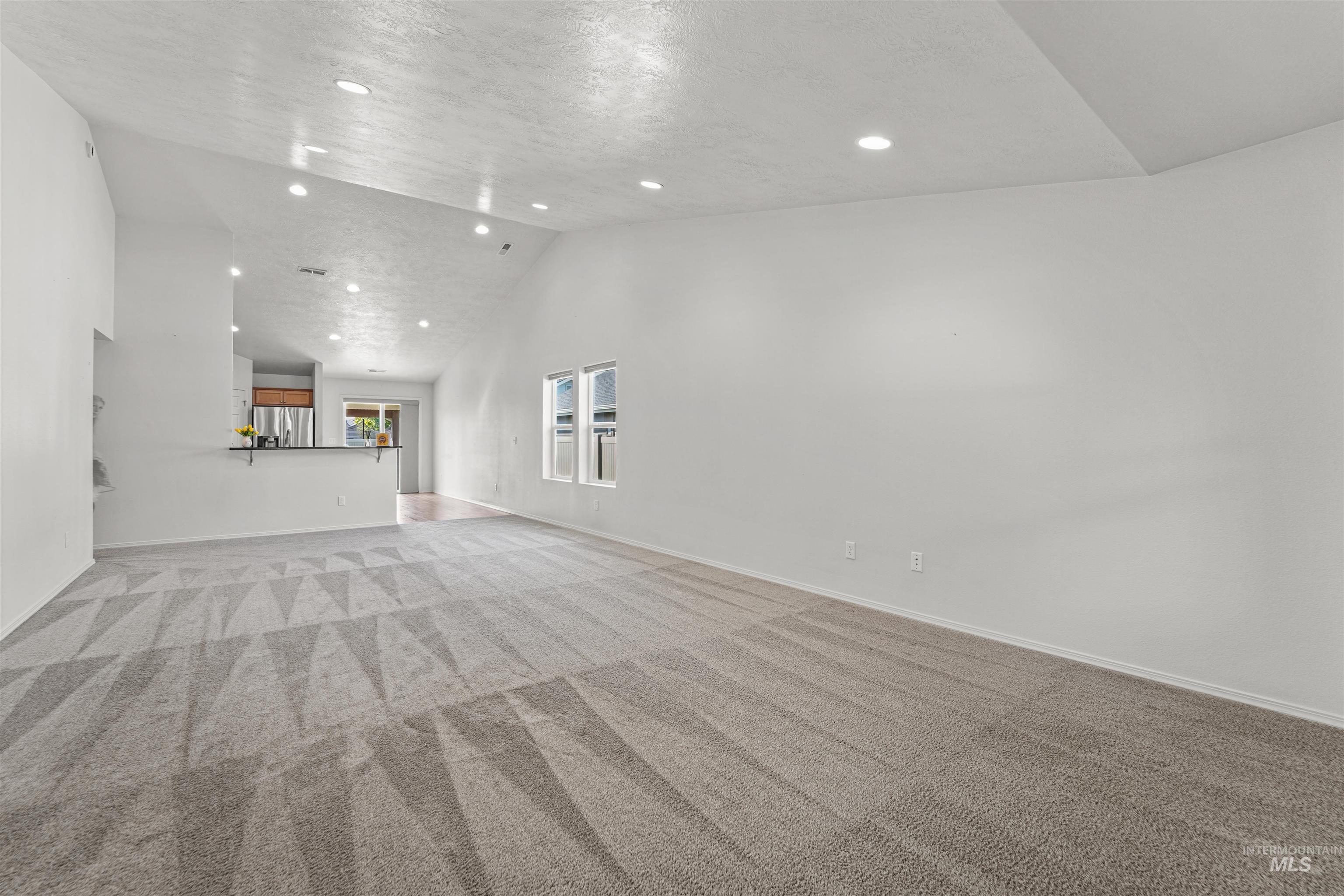 Unfurnished living room with light colored carpet, recessed lighting, a textured ceiling, and high vaulted ceiling