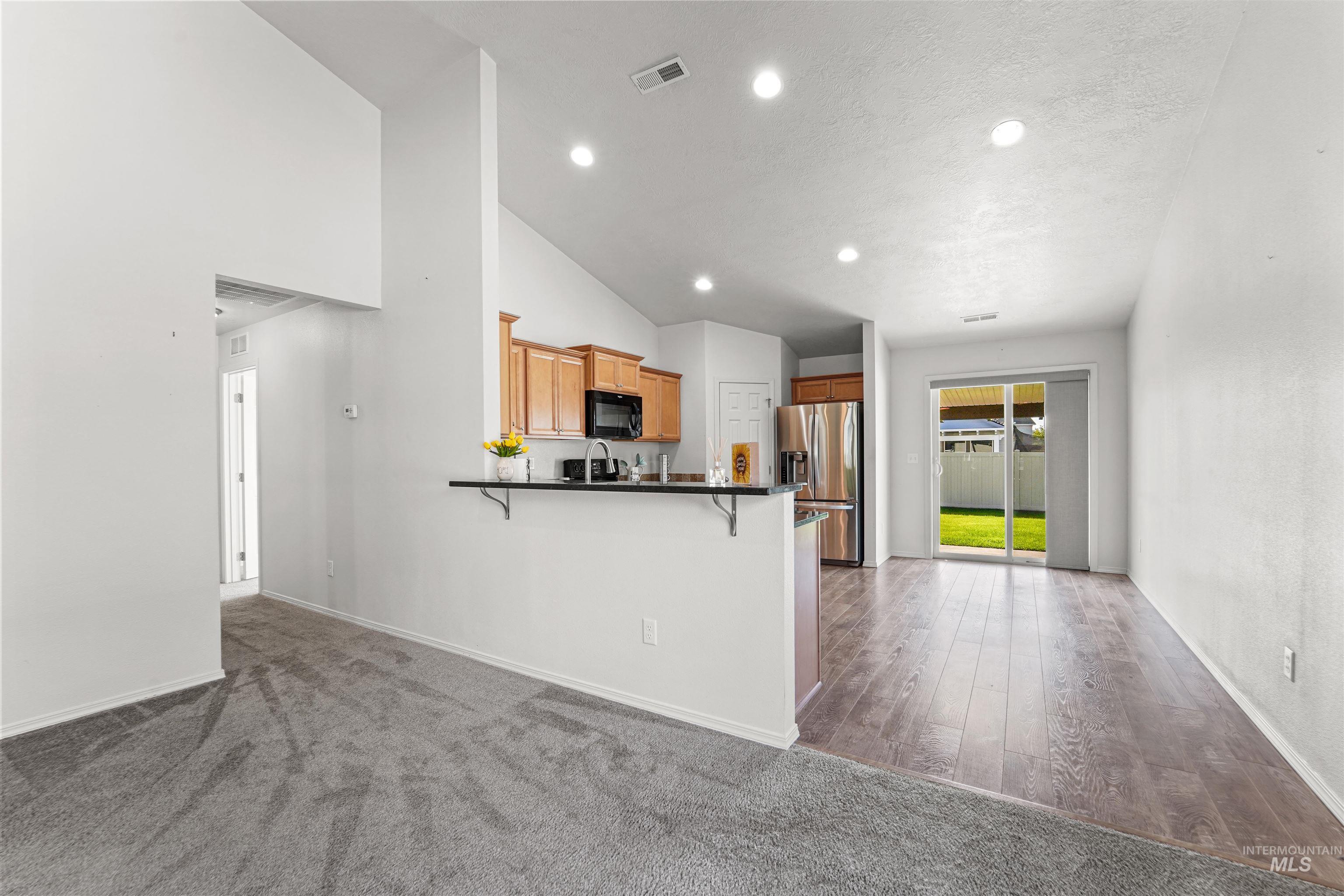 Kitchen featuring stainless steel fridge with ice dispenser, a kitchen breakfast bar, dark colored carpet, black microwave, and recessed lighting