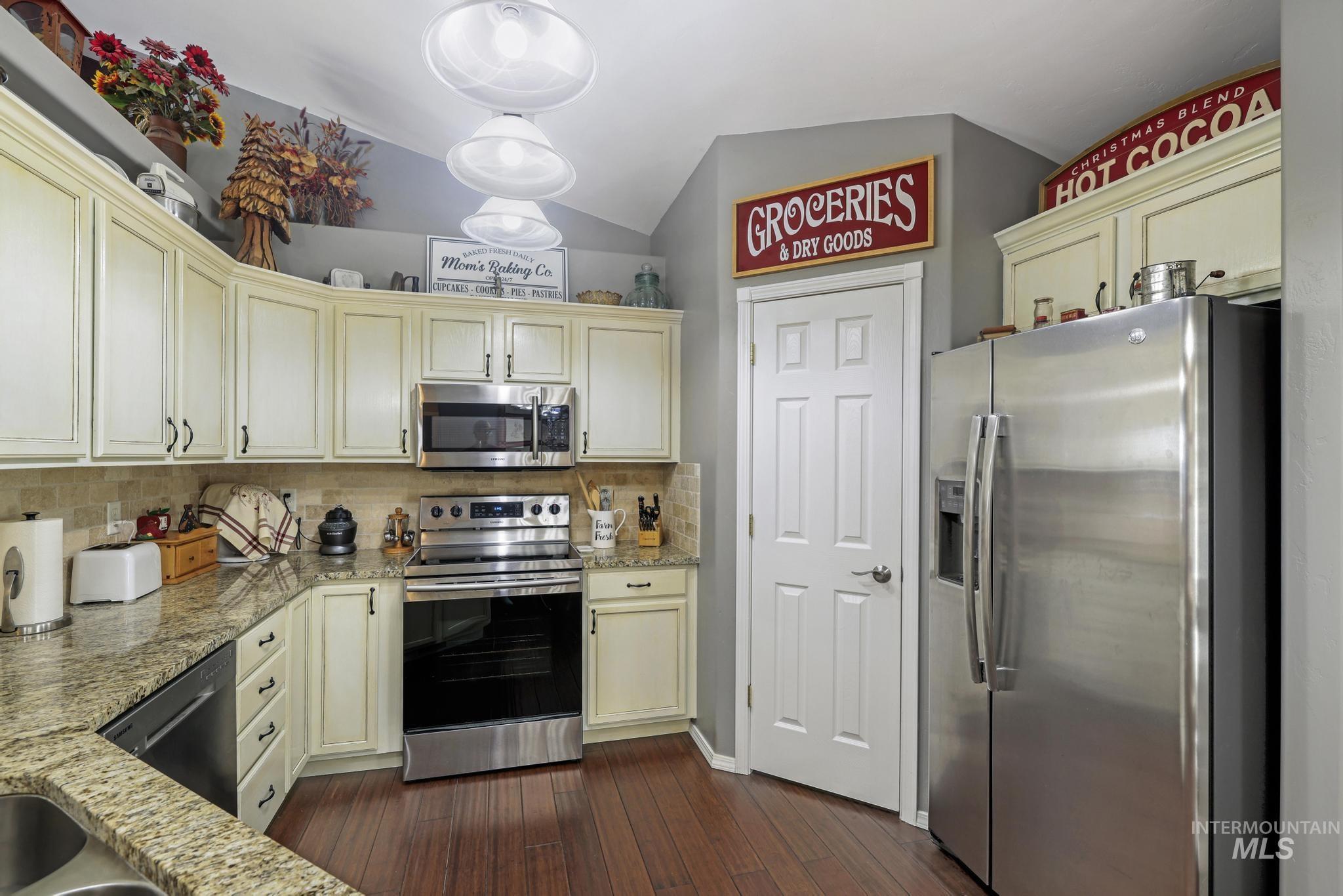 Kitchen featuring stainless steel appliances, light stone countertops, decorative backsplash, cream cabinetry, and vaulted ceiling