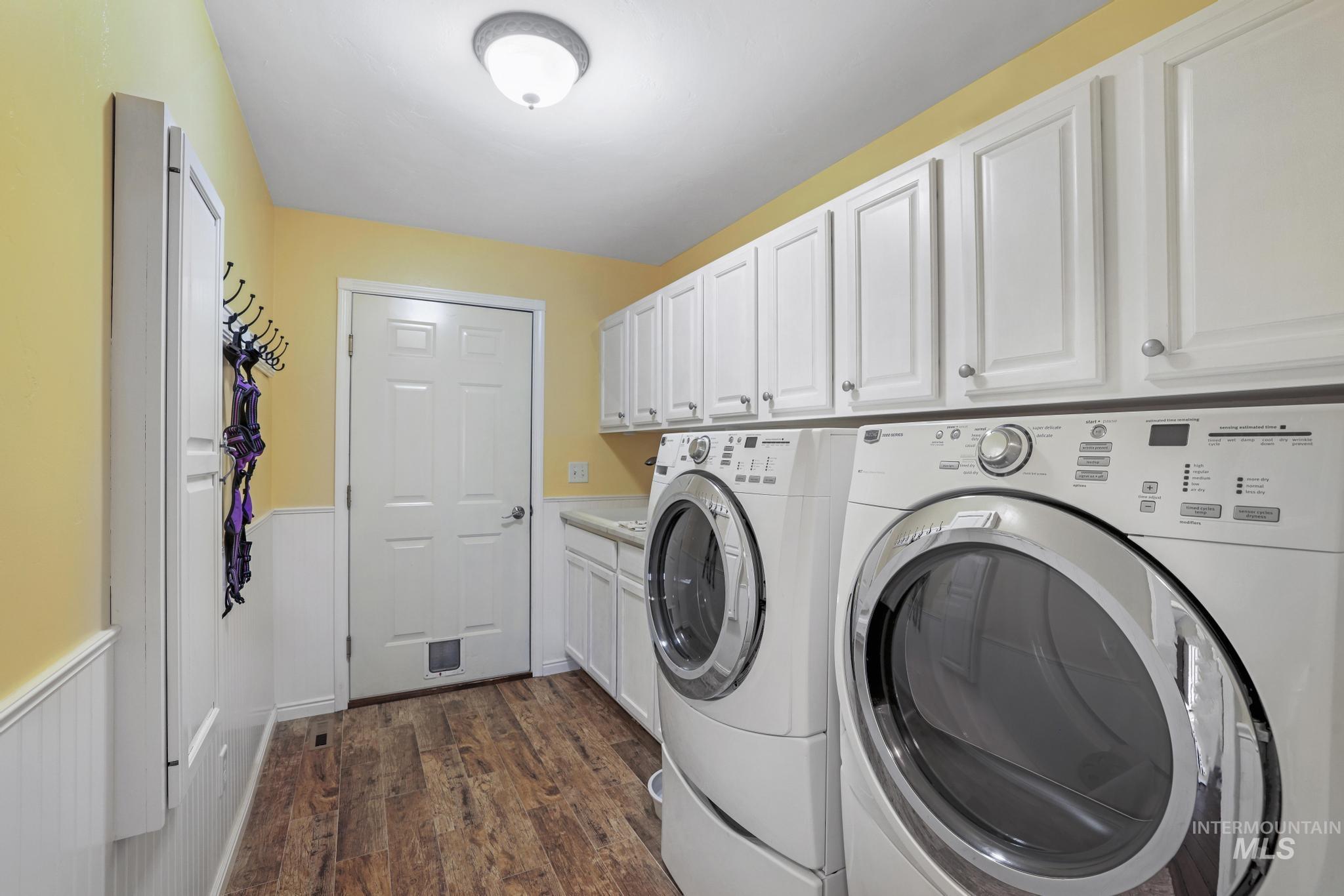 Laundry room featuring a wainscoted wall, dark wood finished floors, washer and clothes dryer, and cabinet space