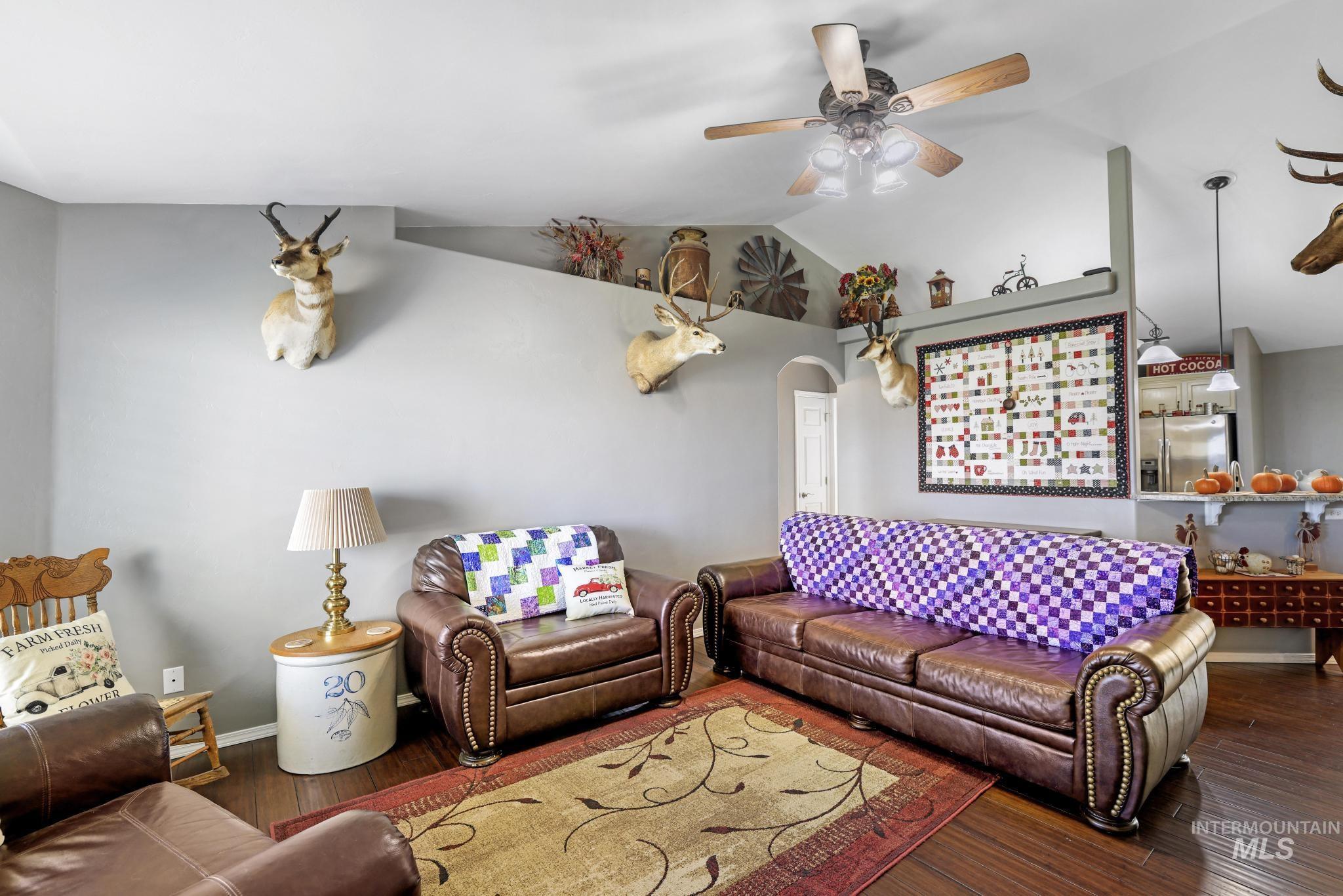 Living room featuring vaulted ceiling, wood finished floors, arched walkways, and ceiling fan