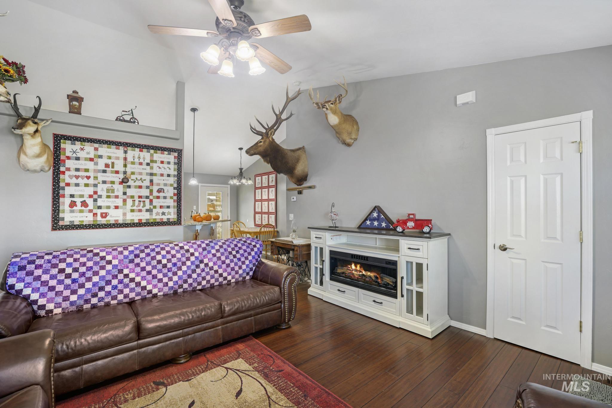 Living room with lofted ceiling, a lit fireplace, dark wood-type flooring, and a ceiling fan
