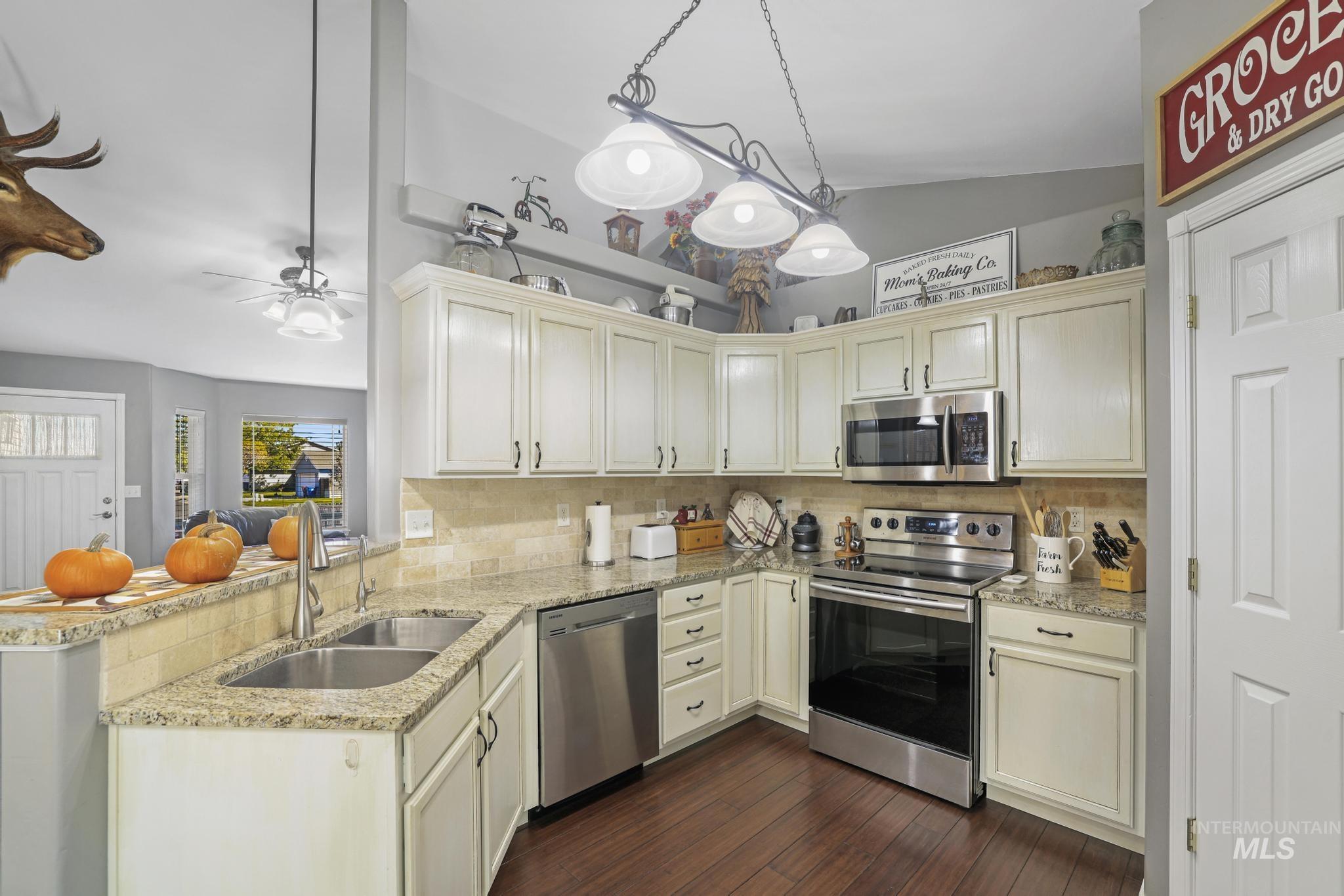 Kitchen featuring appliances with stainless steel finishes, pendant lighting, light stone counters, dark wood-type flooring, and lofted ceiling