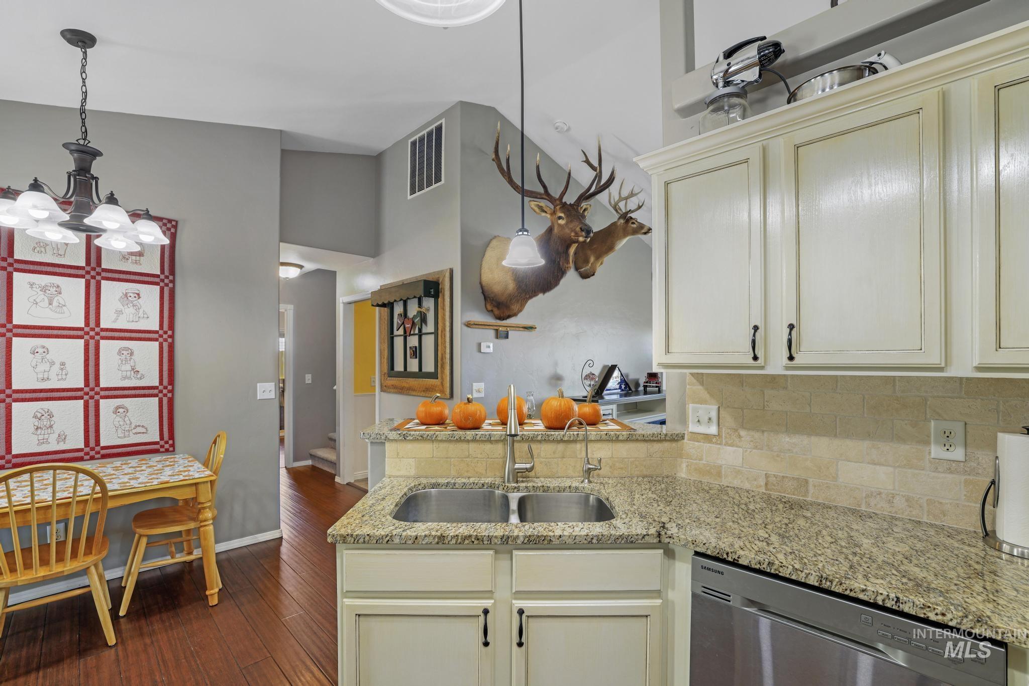 Kitchen featuring a peninsula, dishwasher, dark wood finished floors, decorative light fixtures, and light stone countertops