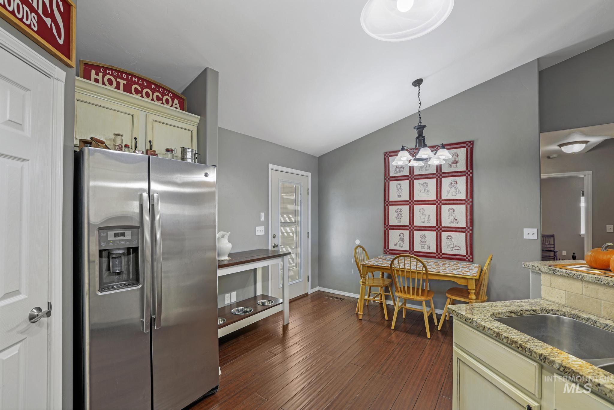 Kitchen with stainless steel fridge with ice dispenser, vaulted ceiling, light stone countertops, dark wood-style flooring, and hanging light fixtures