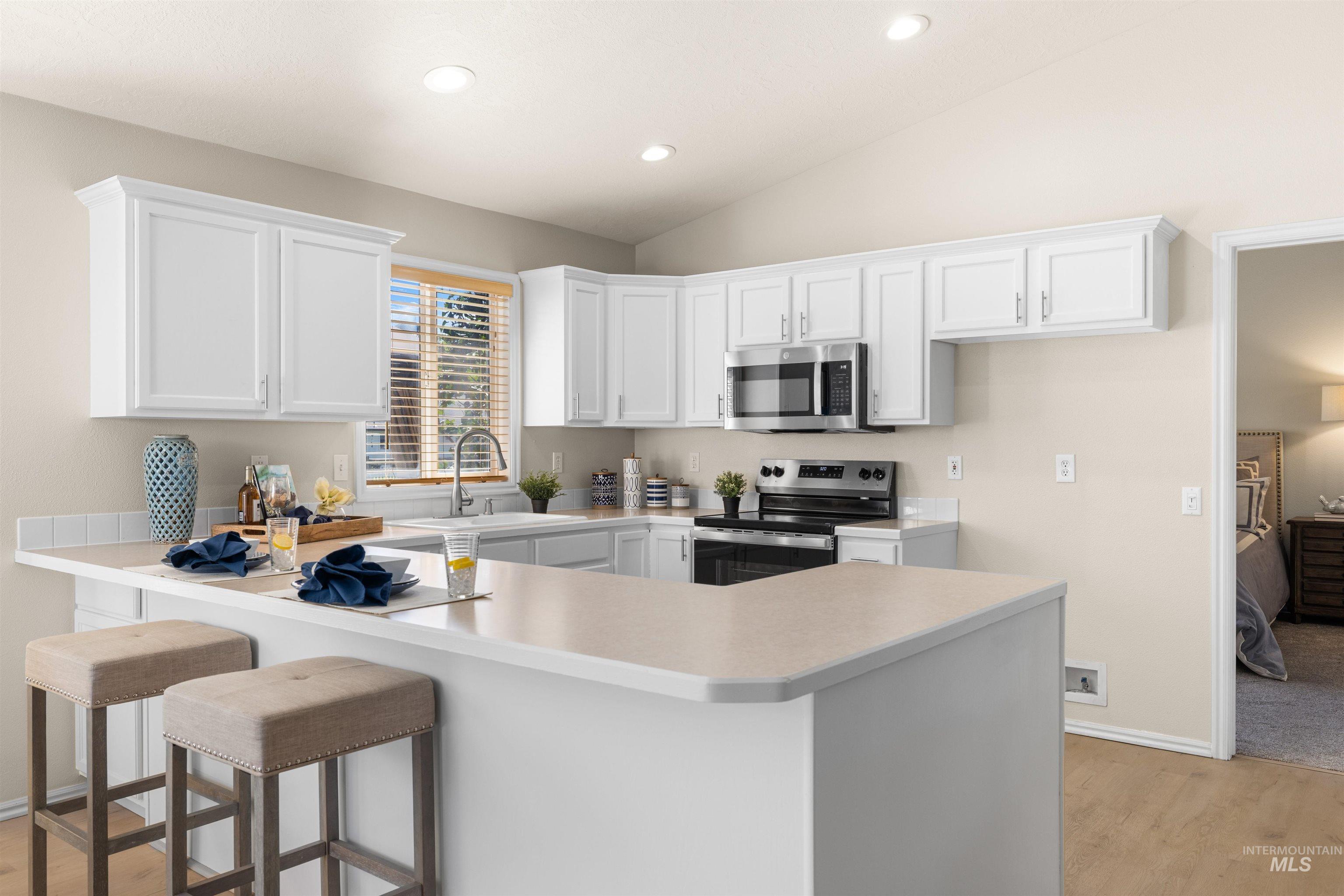 Kitchen featuring stainless steel appliances, a peninsula, light wood-type flooring, white cabinets, and lofted ceiling