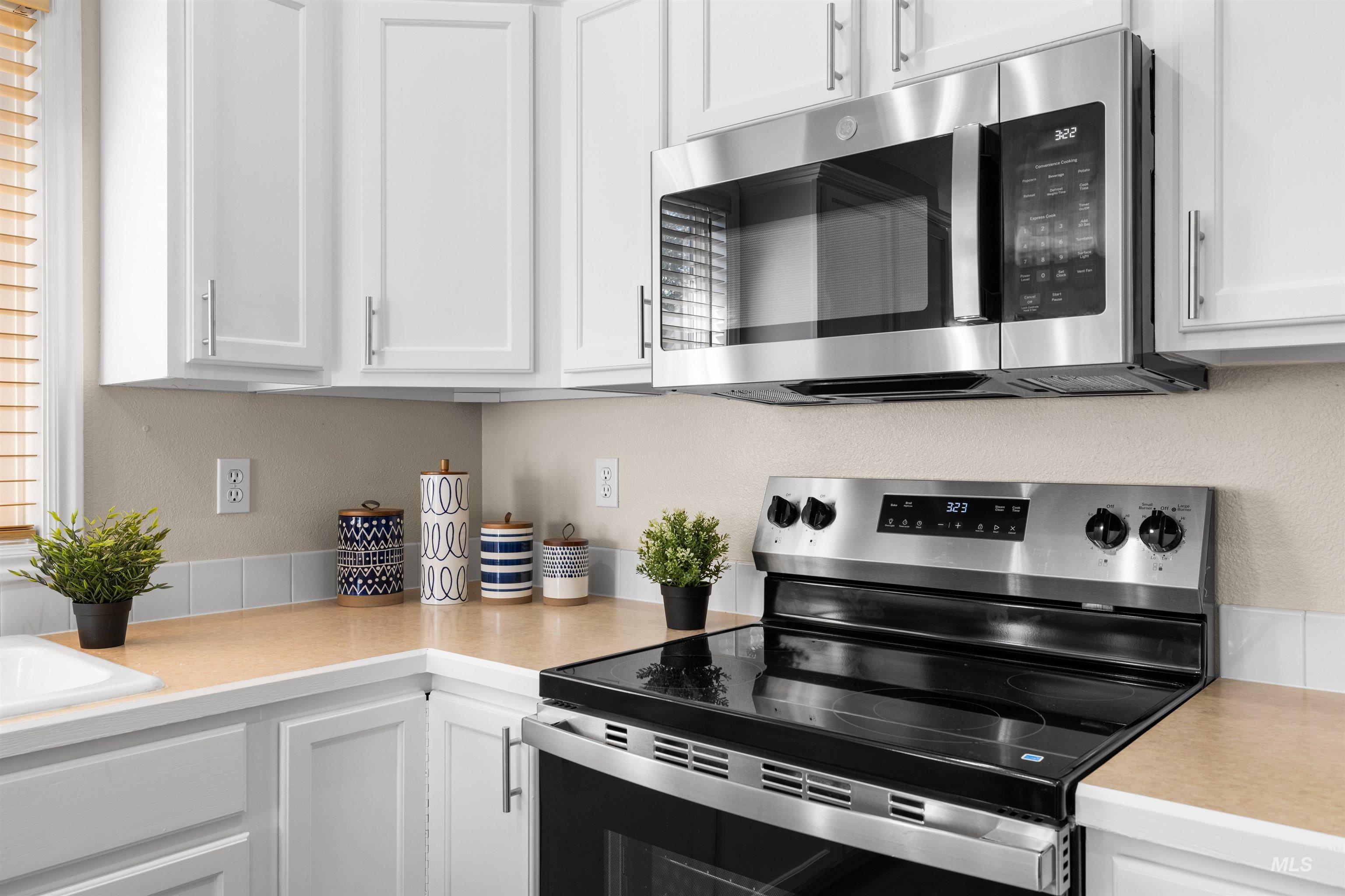 Kitchen with stainless steel appliances, light countertops, white cabinetry, and a textured wall