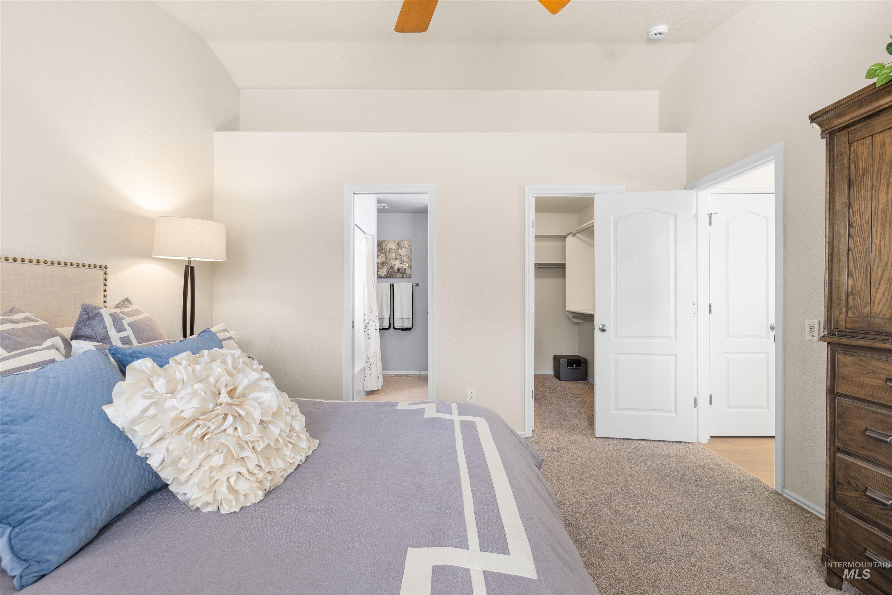Bedroom featuring light colored carpet, a ceiling fan, ensuite bathroom, and a spacious closet