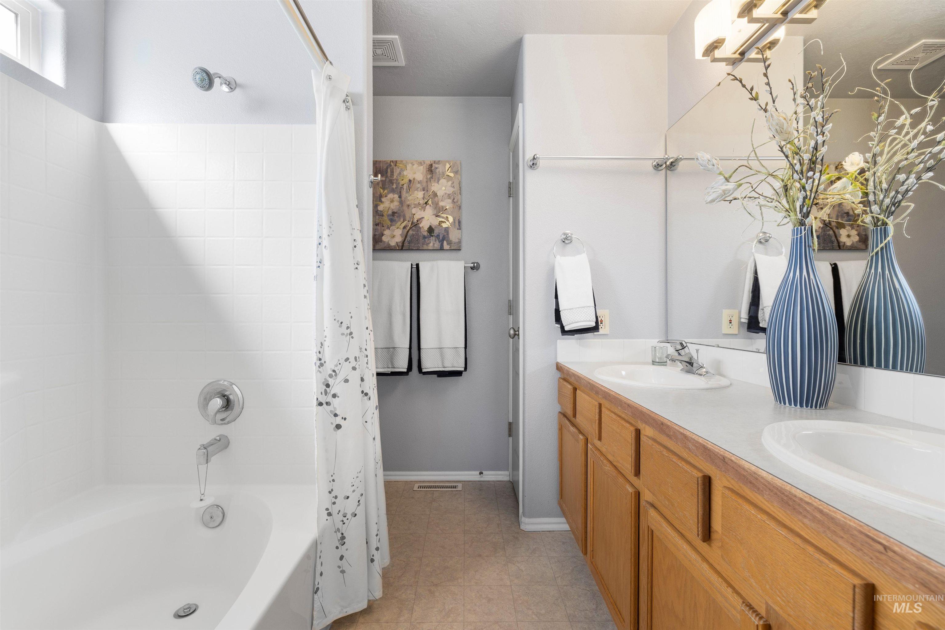 Bathroom with shower / bathtub combination with curtain and double vanity