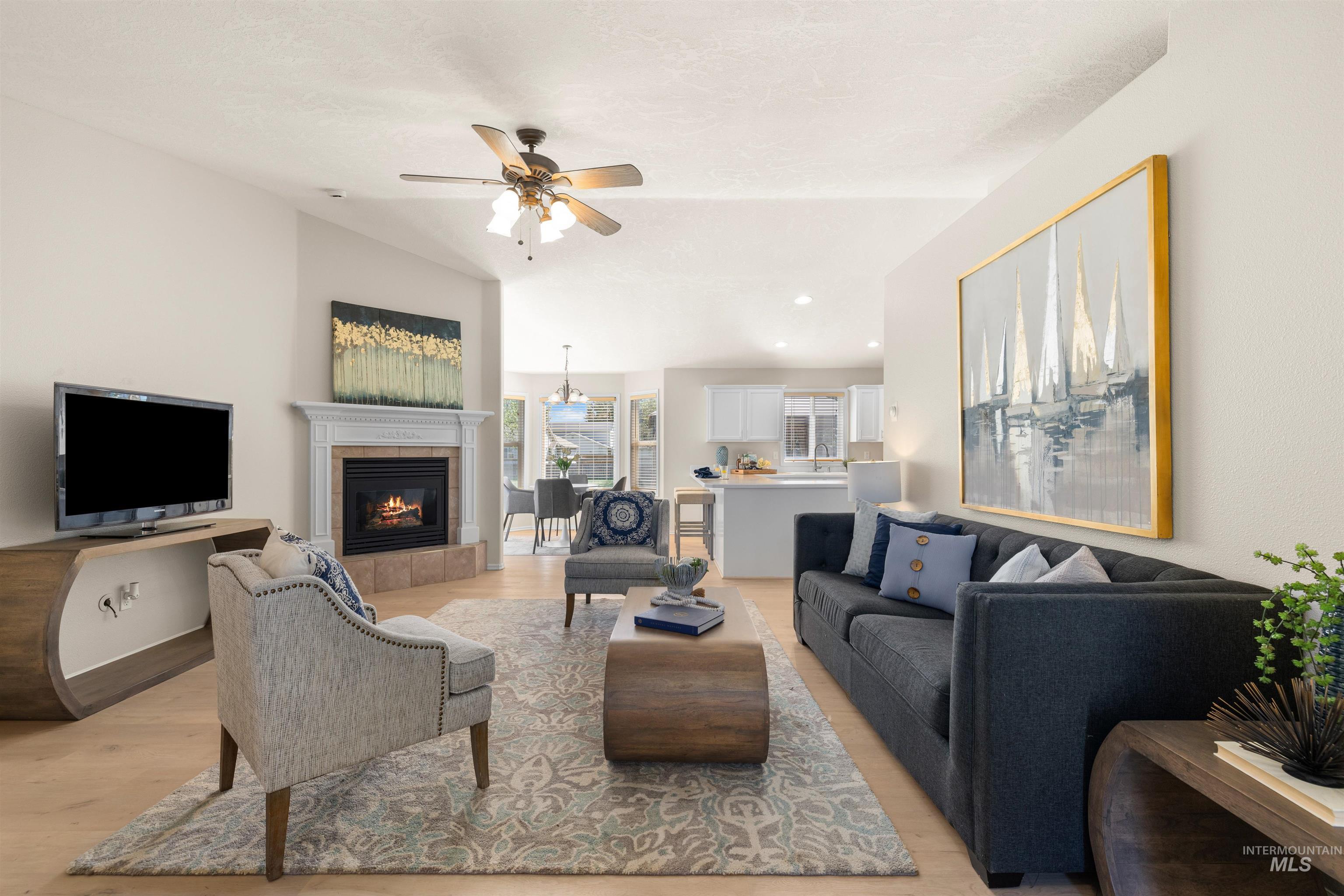 Living room featuring light wood finished floors, a tiled fireplace, ceiling fan, recessed lighting, and vaulted ceiling