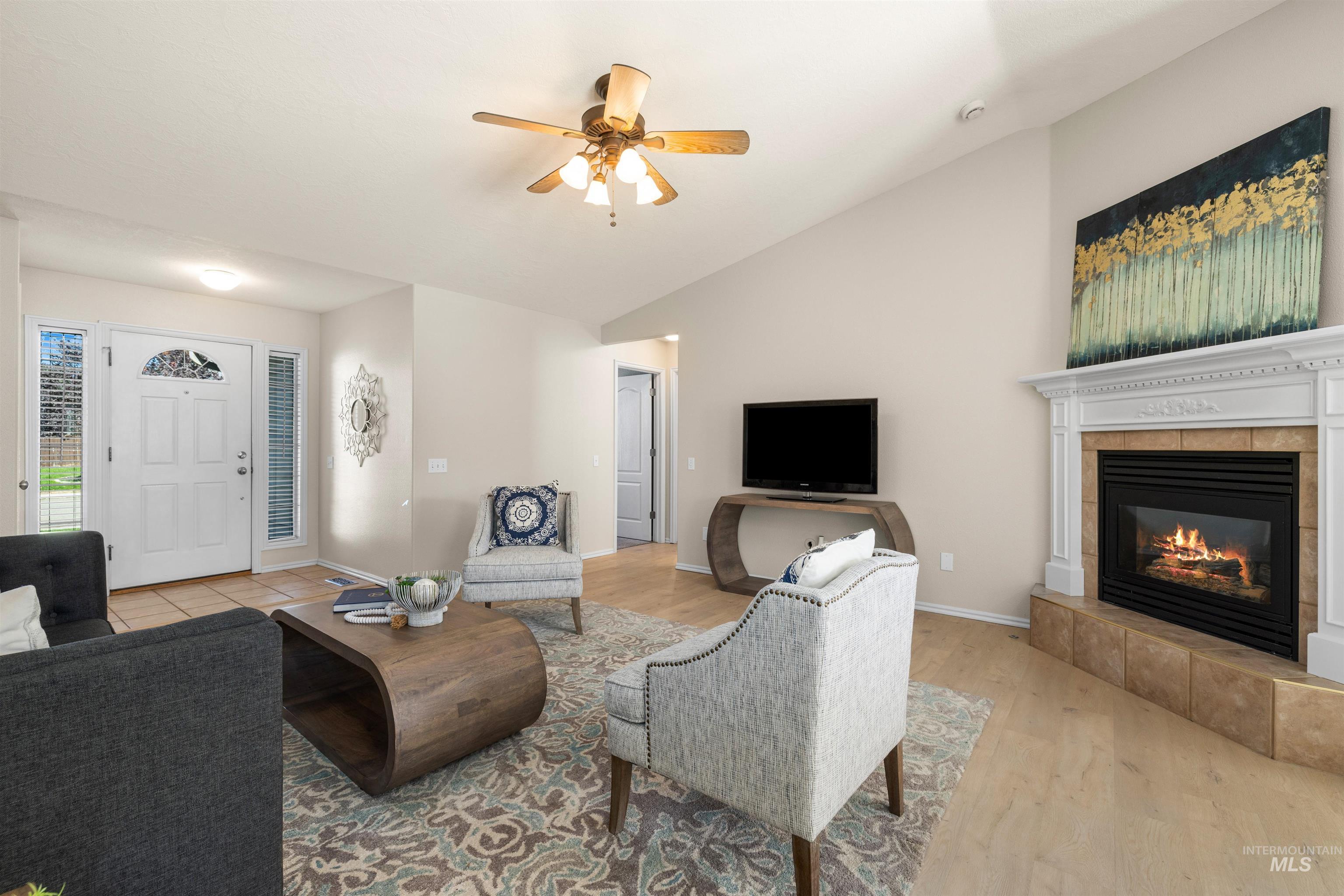 Living room featuring vaulted ceiling, light wood finished floors, ceiling fan, and a fireplace