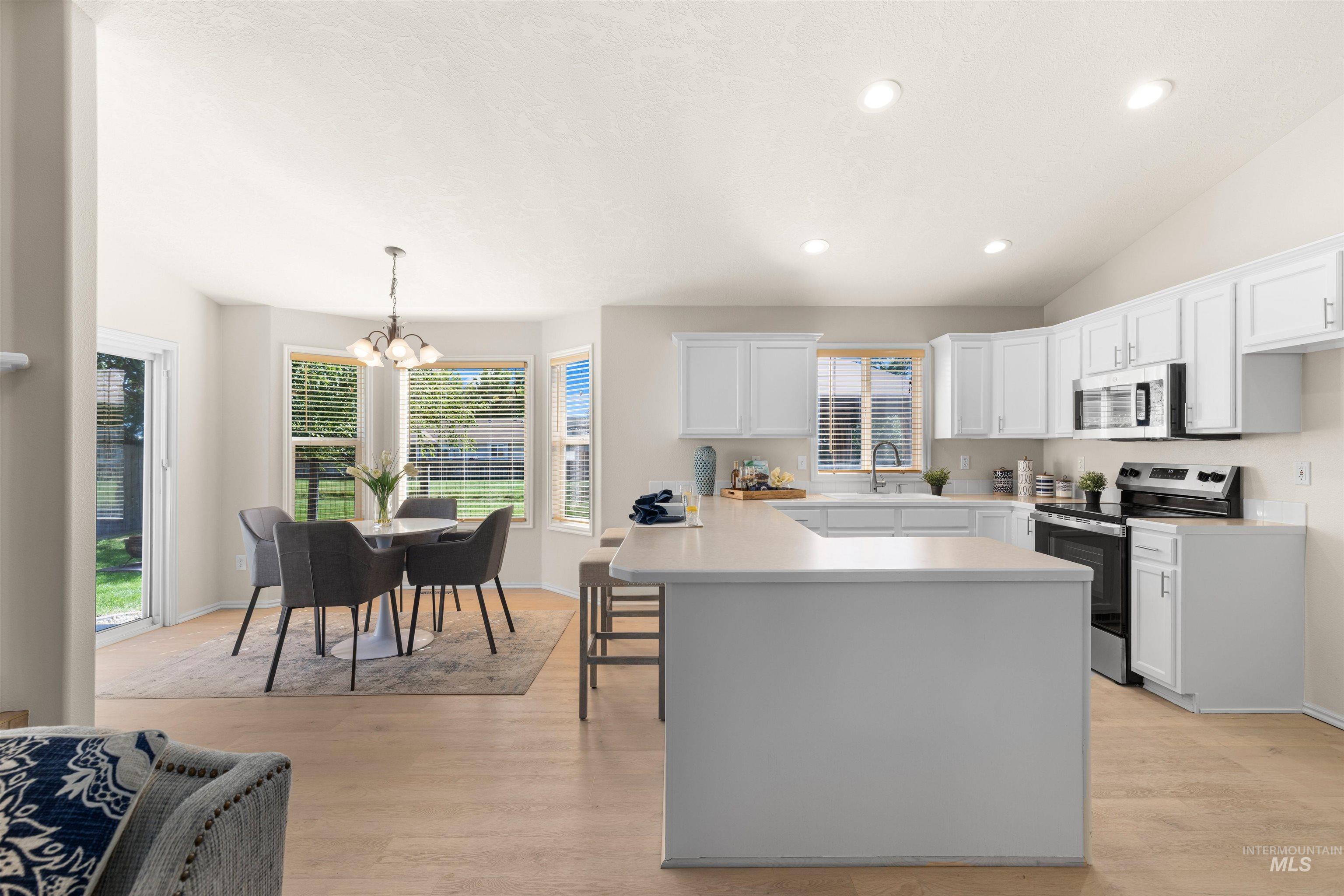 Kitchen with light countertops, stainless steel appliances, white cabinetry, hanging light fixtures, and light wood finished floors
