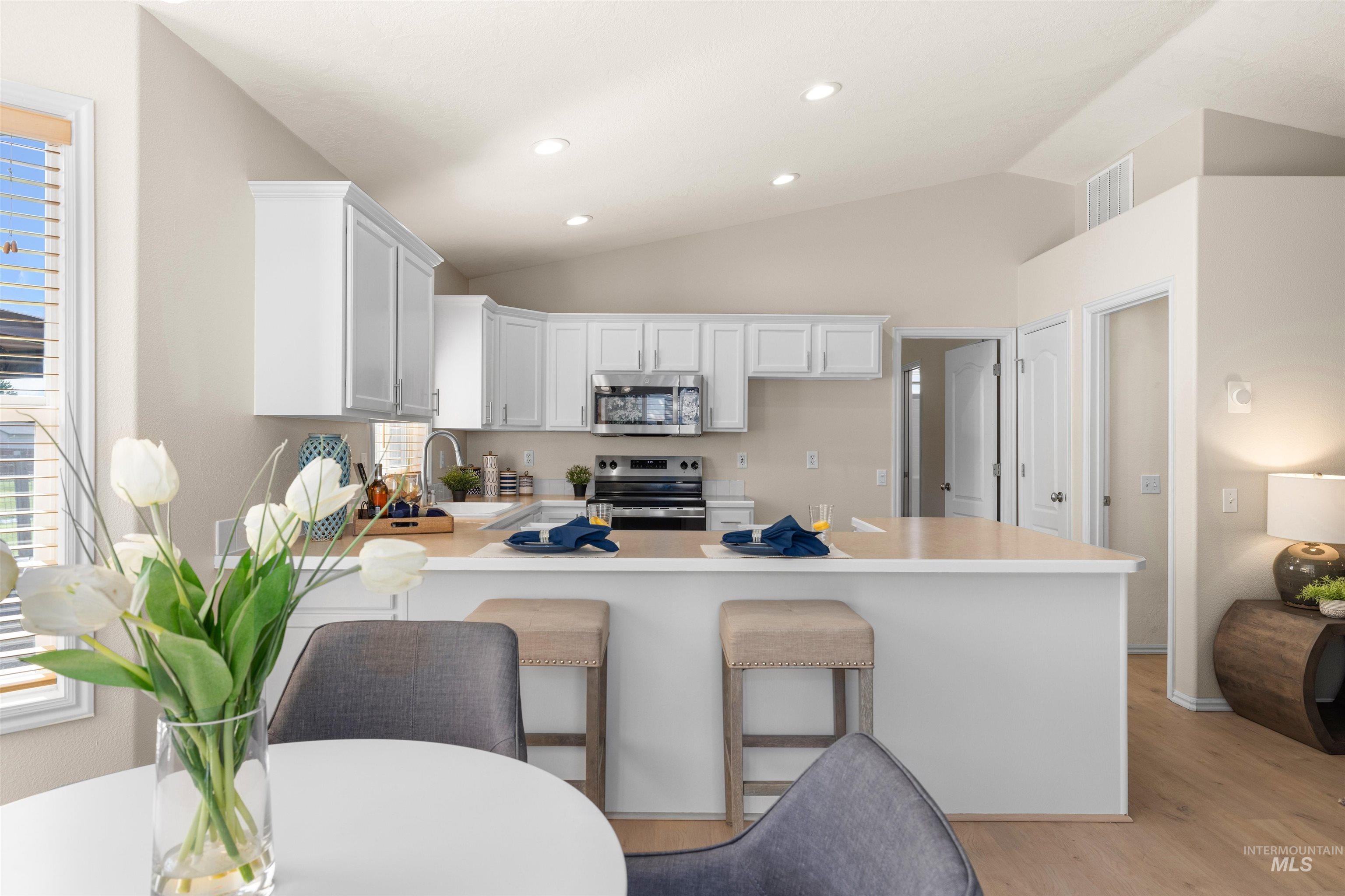 Kitchen featuring a kitchen breakfast bar, light countertops, white cabinets, appliances with stainless steel finishes, and a peninsula