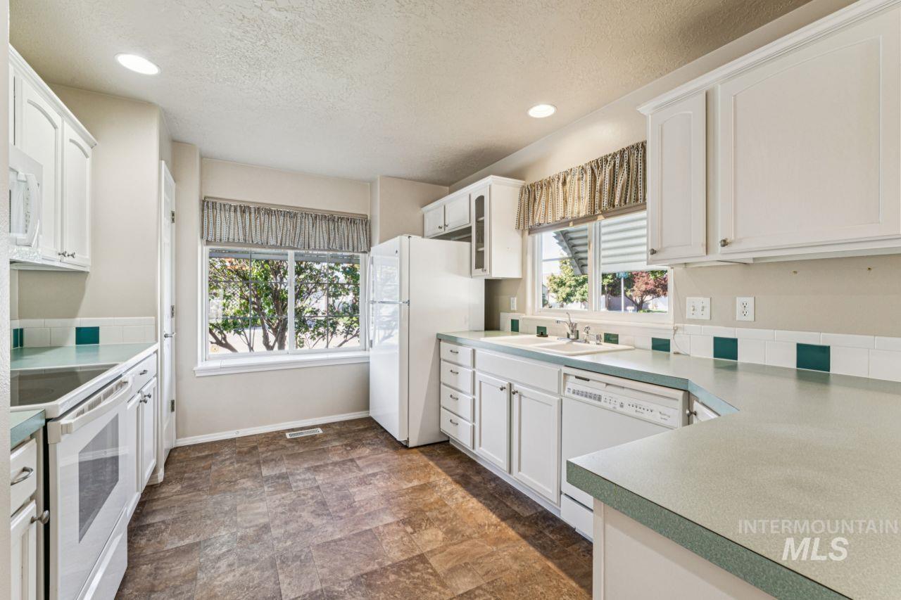 Kitchen featuring white appliances, white cabinetry, recessed lighting, stone finish flooring, and a textured ceiling