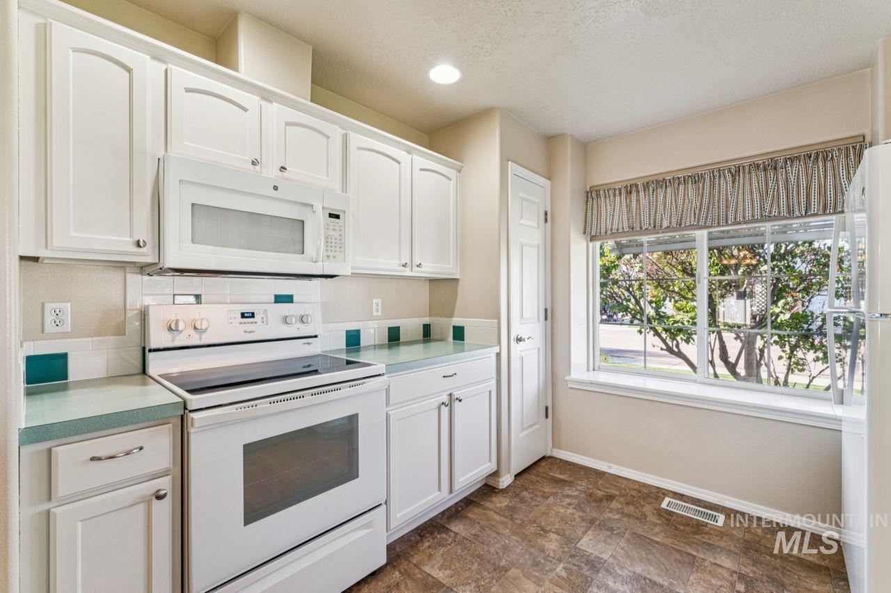 Kitchen featuring white appliances, white cabinetry, stone finish flooring, light countertops, and recessed lighting